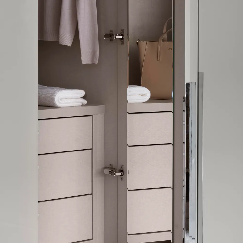 Open wardrobe doors showing taupe drawers, folded towels and a handbag