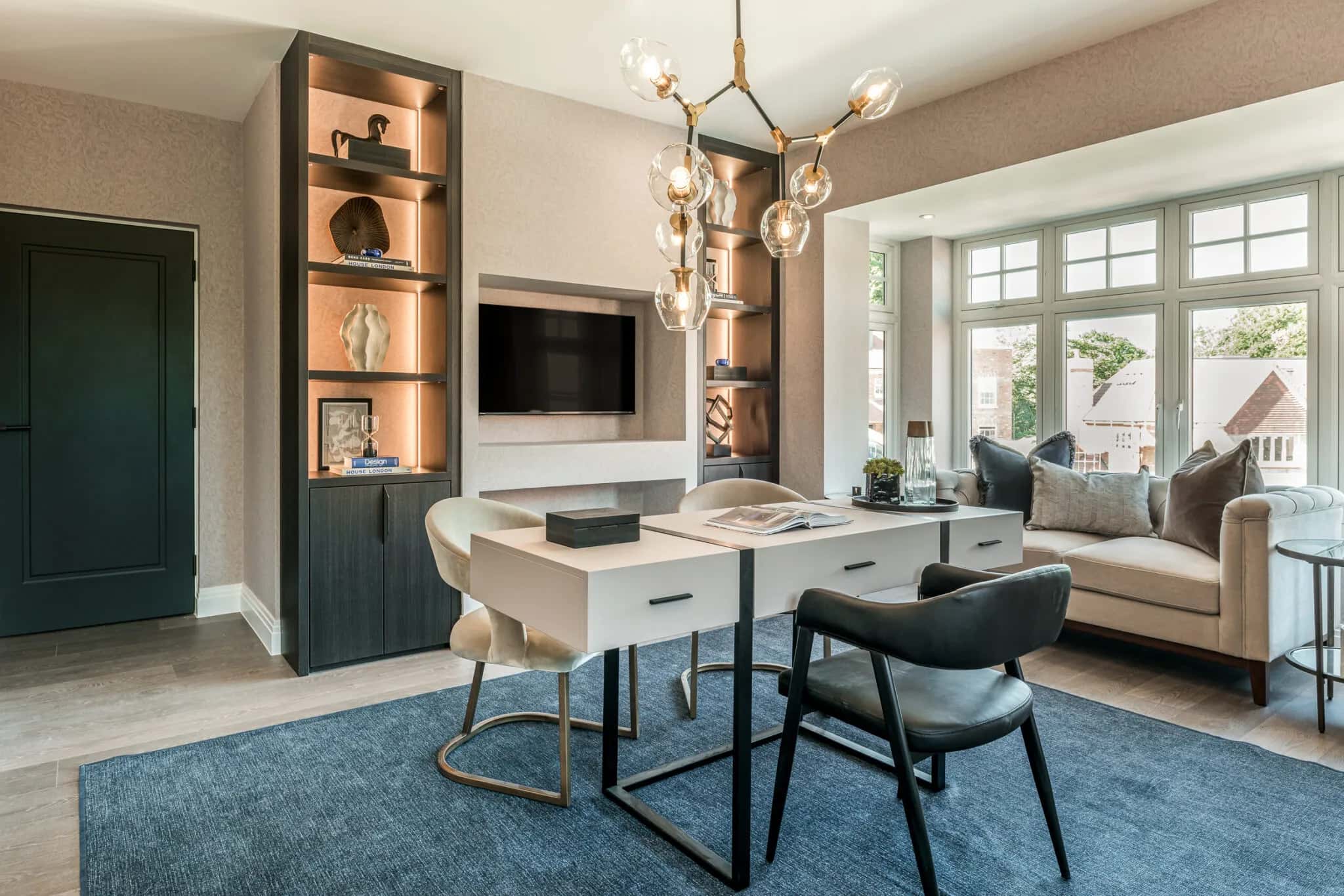 Home office with dark oak shelving unit, wall-mounted TV, white desk and chairs, and bay window seating