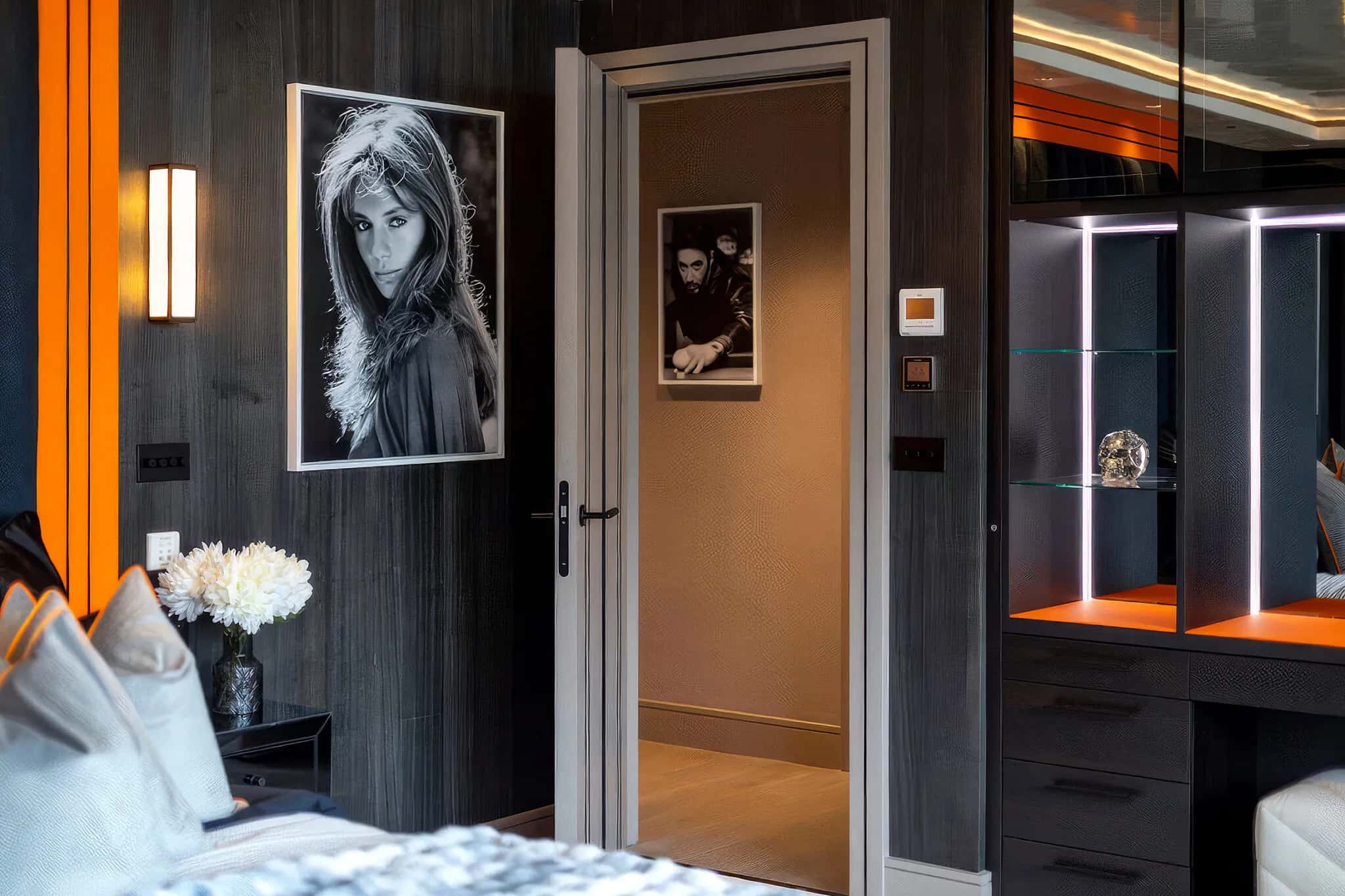Bedroom doorway beside a monochrome portrait and a lit dressing unit with mirrored shelves
