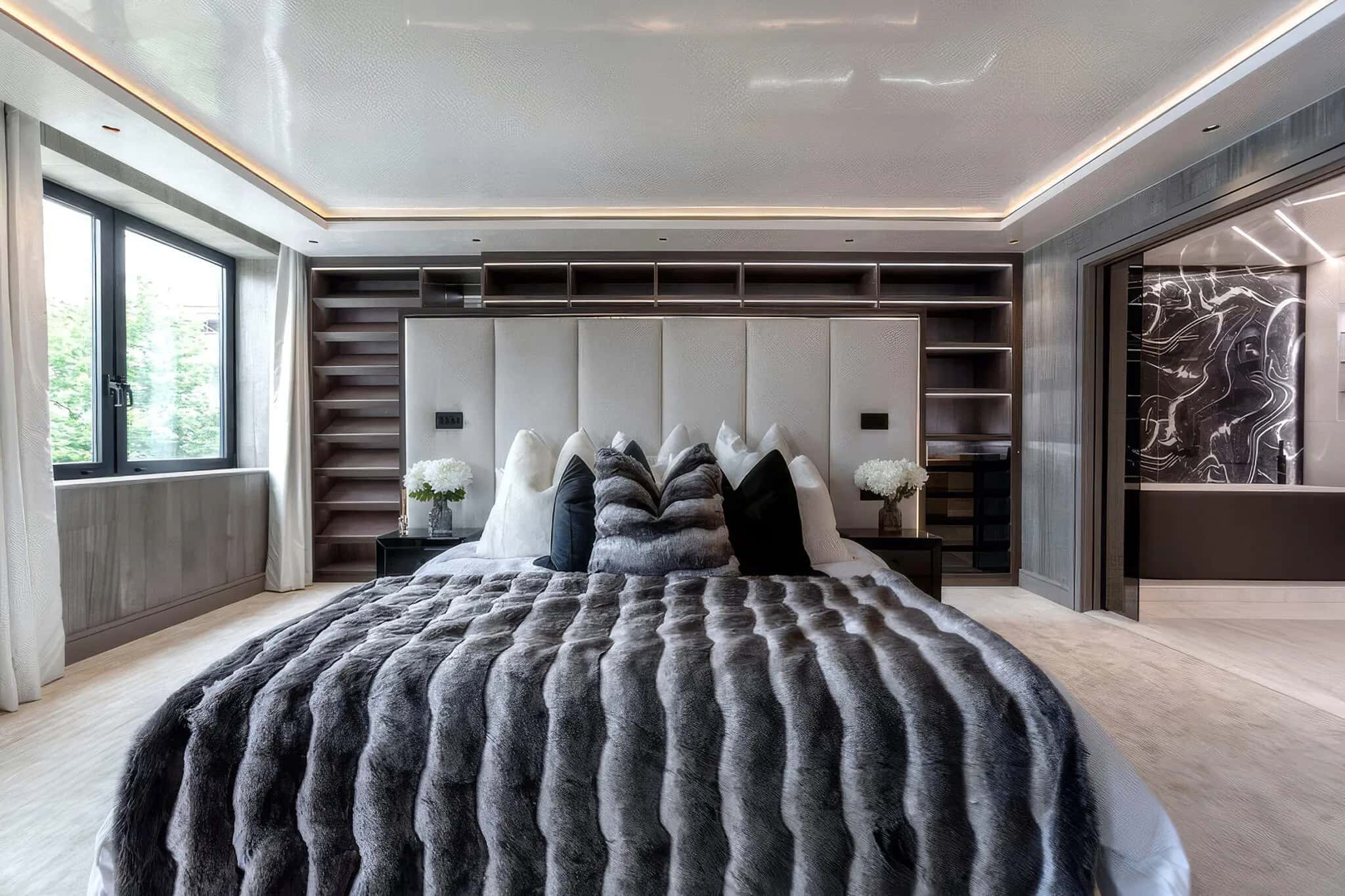 Bedroom with fitted shelving behind a cushioned headboard and marble-effect dressing area beyond