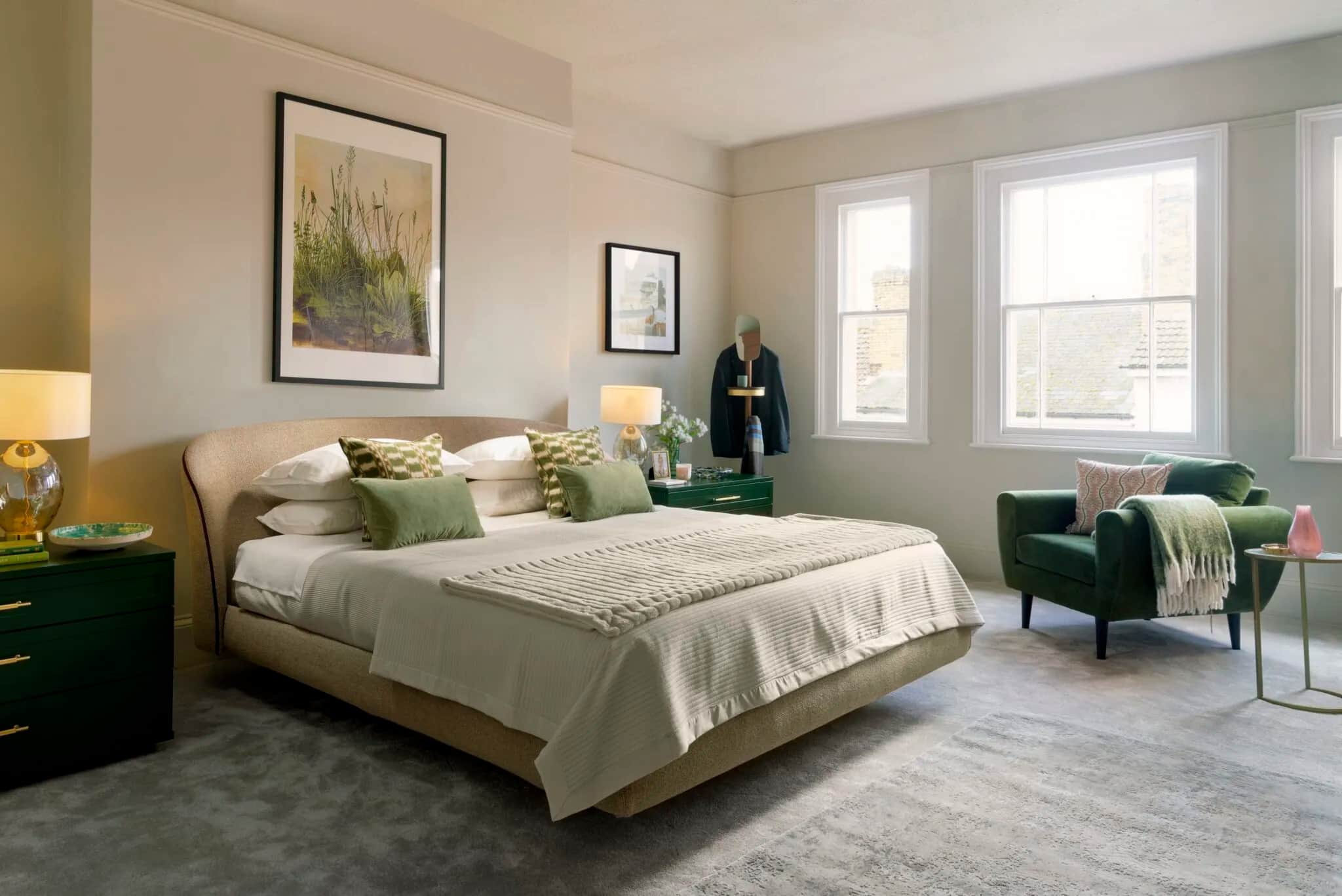 Bedroom with upholstered bed, green armchair and green bedside chests beside sash windows