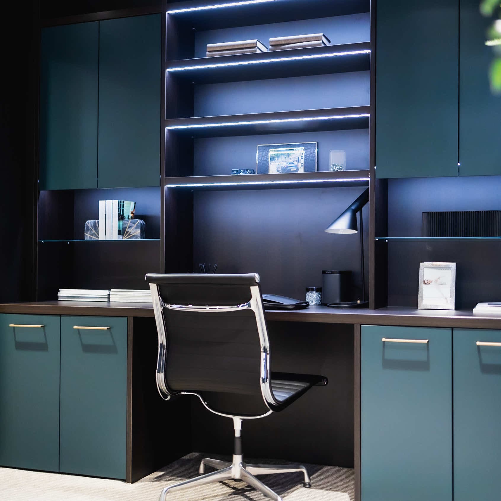 Home office with dark oak shelves, inlaid LED lighting and green cabinets around a desk