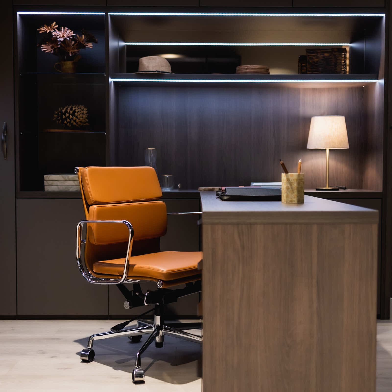 Home study with dark fitted shelving, LED lighting, wooden desk and tan leather chair