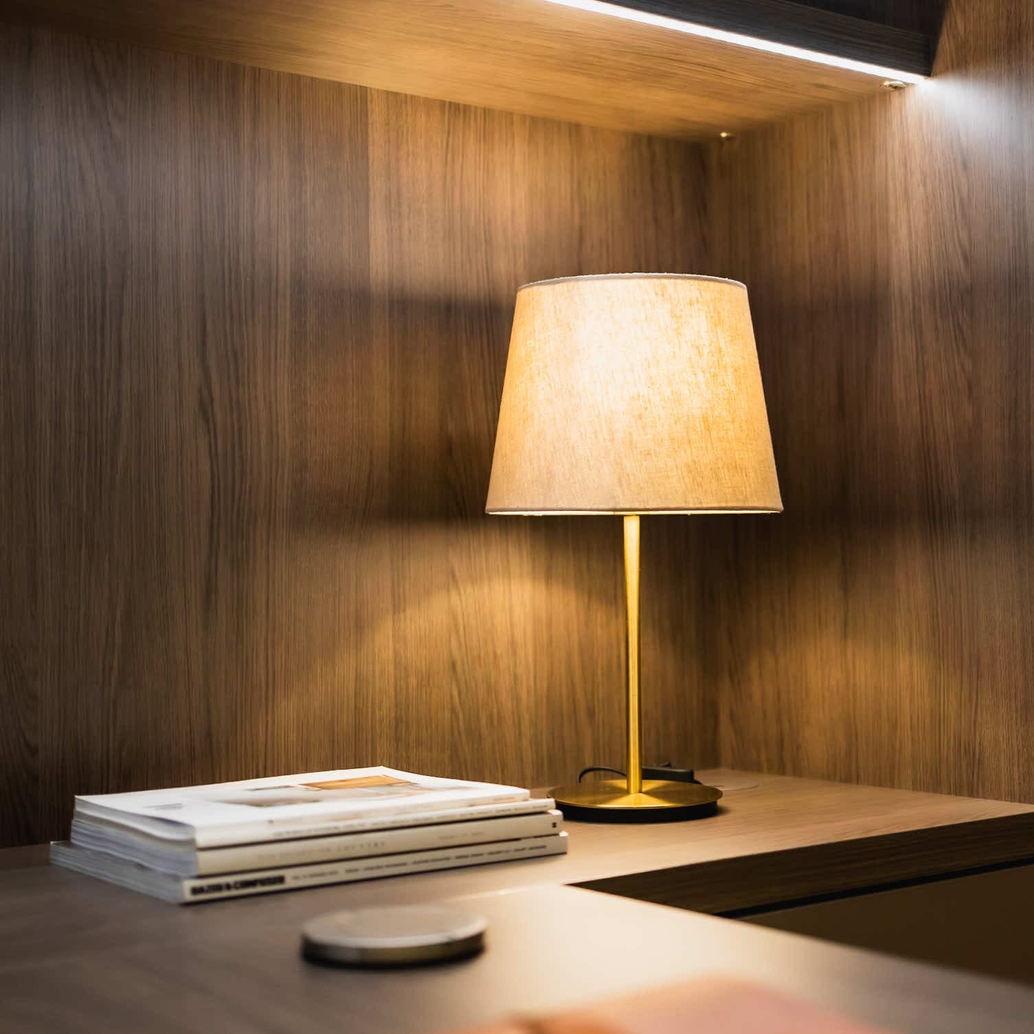 Desk lamp and magazines on a wood-panelled study worktop with LED lighting