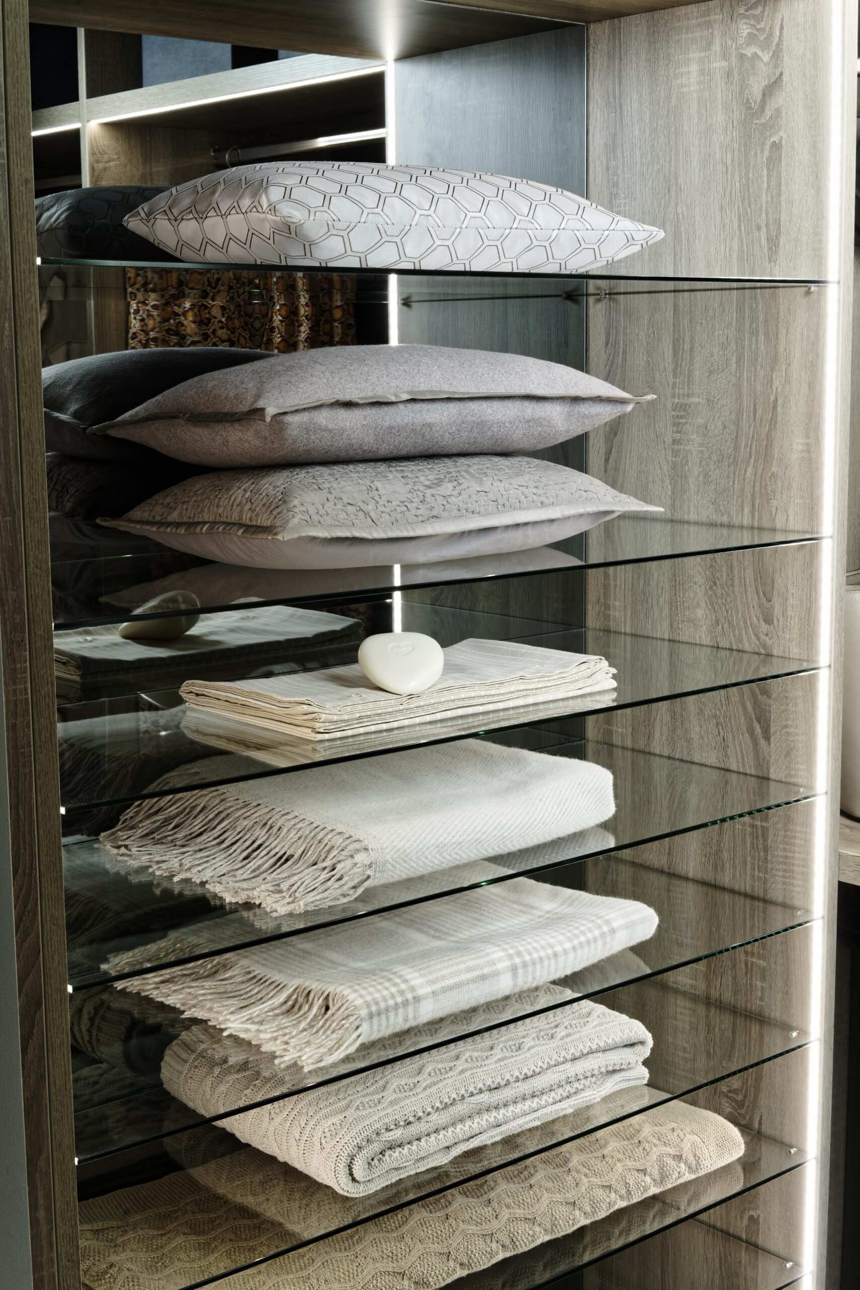 Glass shelving in a wardrobe holding cushions, throws and blankets