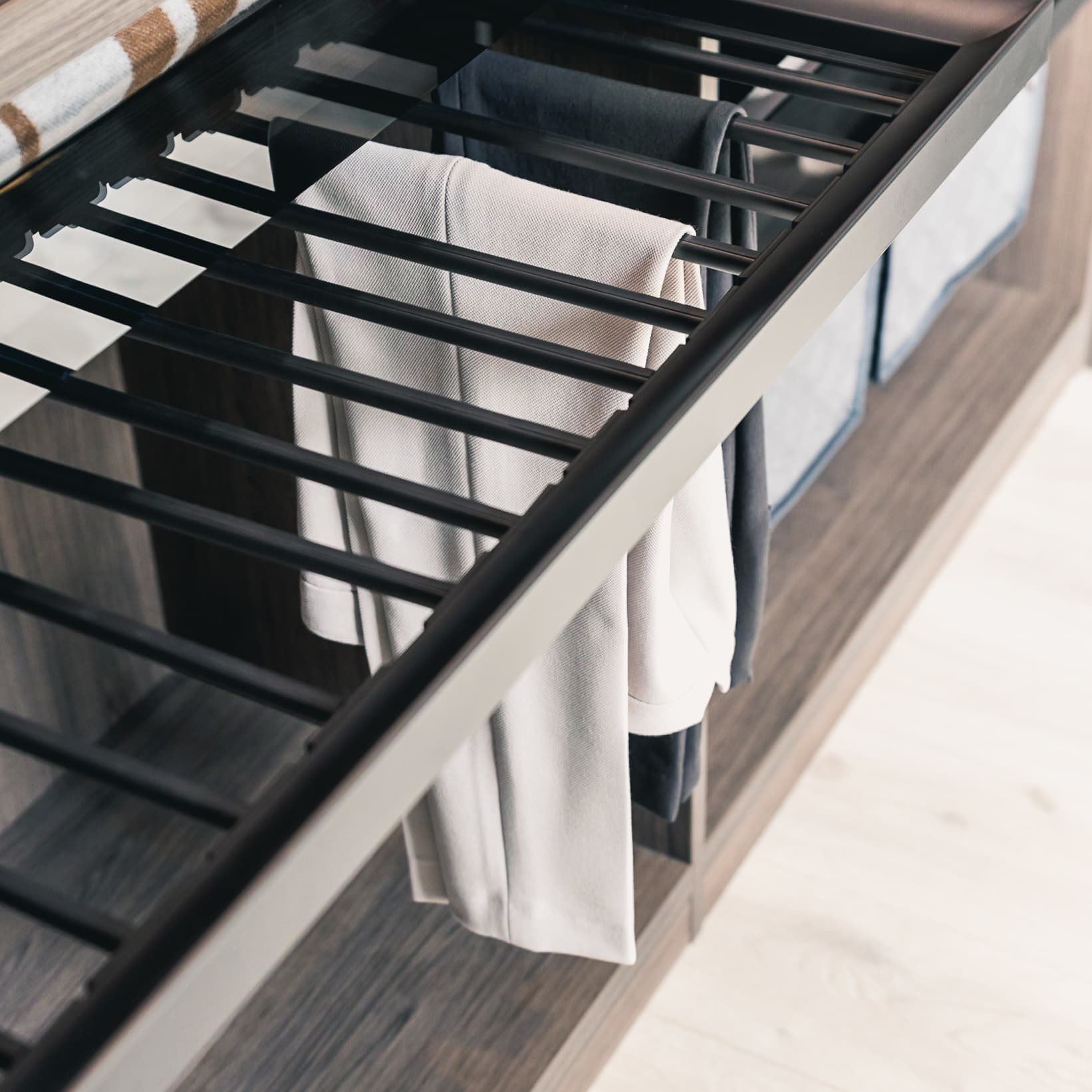 Pull-out trouser rack with dark rails holding folded trousers in a wardrobe