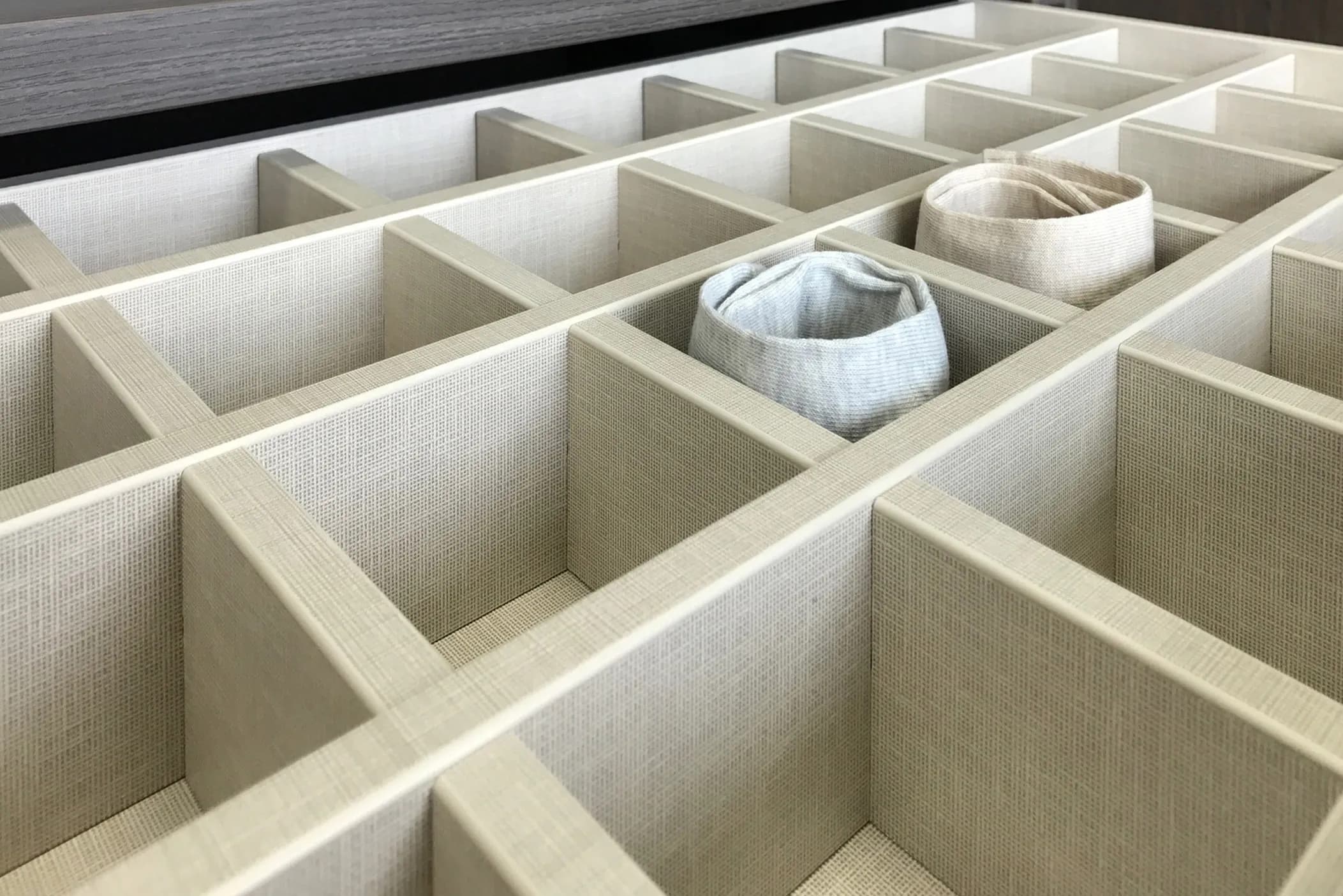 Drawer with fabric-lined compartment dividers holding rolled socks and accessories