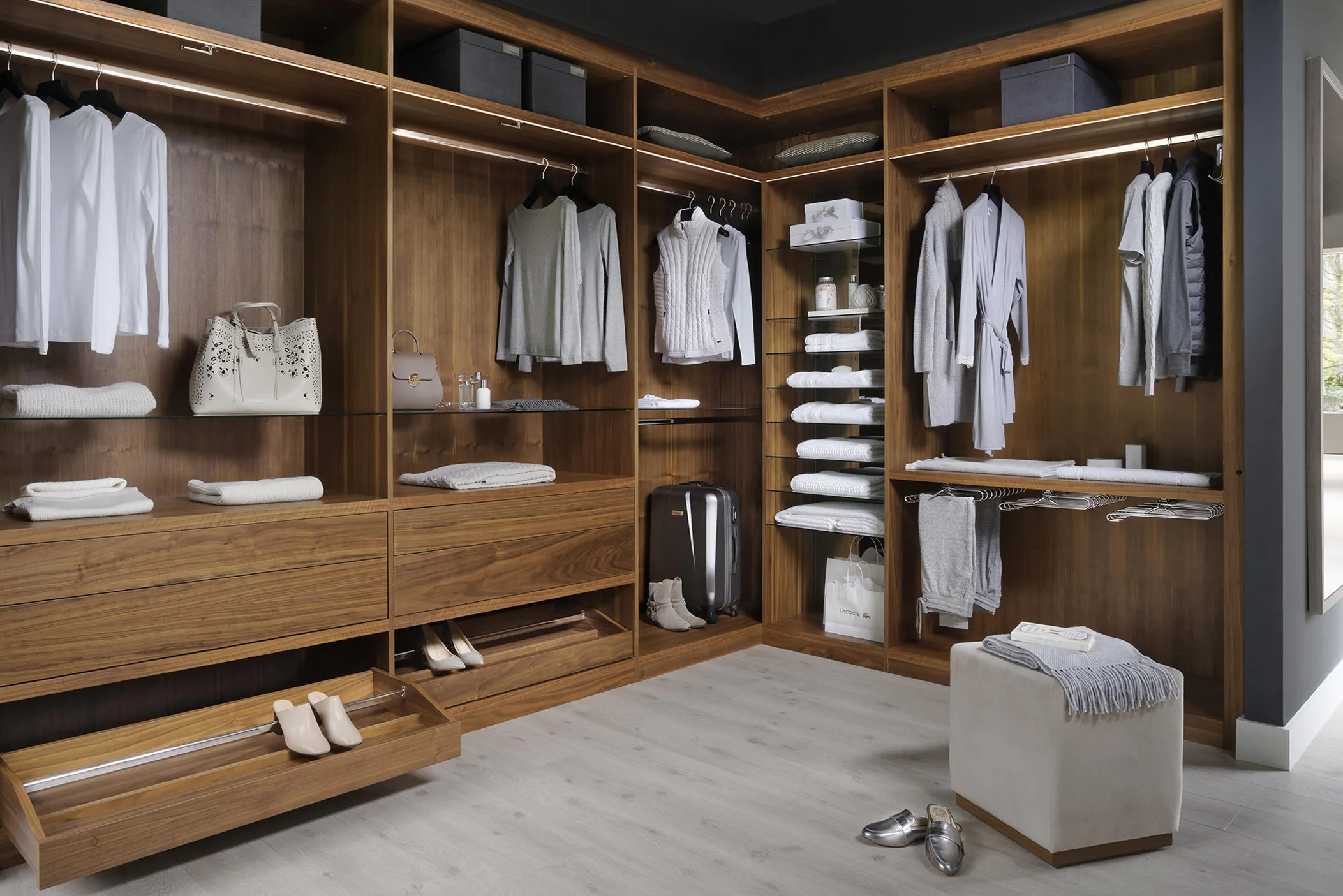 Walnut walk-in wardrobe with corner shelving, hanging rails, pull-out shoe drawer and ottoman