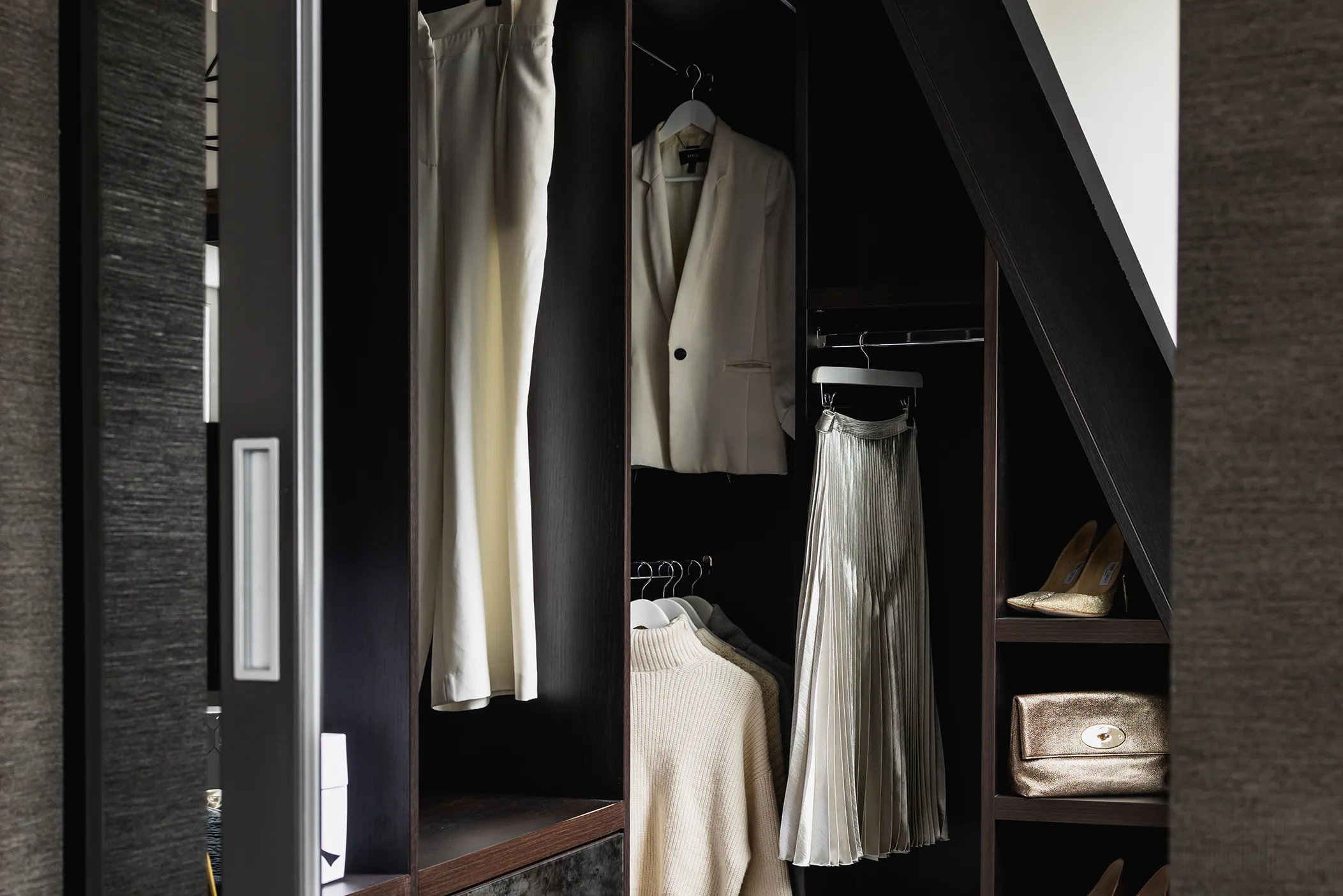 Dark wardrobe under a sloping ceiling with hanging jacket, skirt and shoes