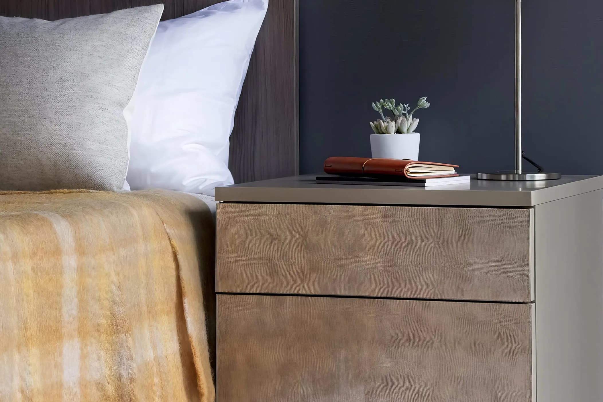 Oak bedside drawers with leather-effect fronts beside a bed with yellow throw