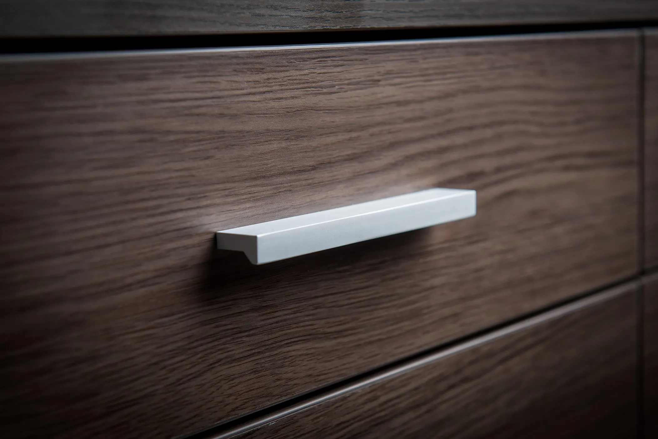 Close-up of a silver bar handle on a dark oak-effect drawer