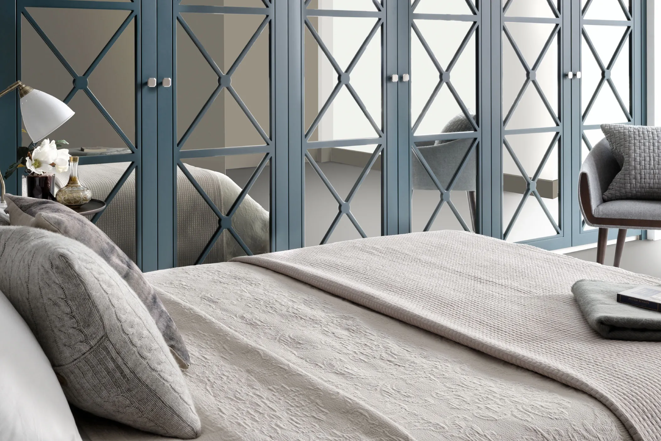 Blue fitted wardrobe with lattice mirrored doors beside a bed with grey bedding