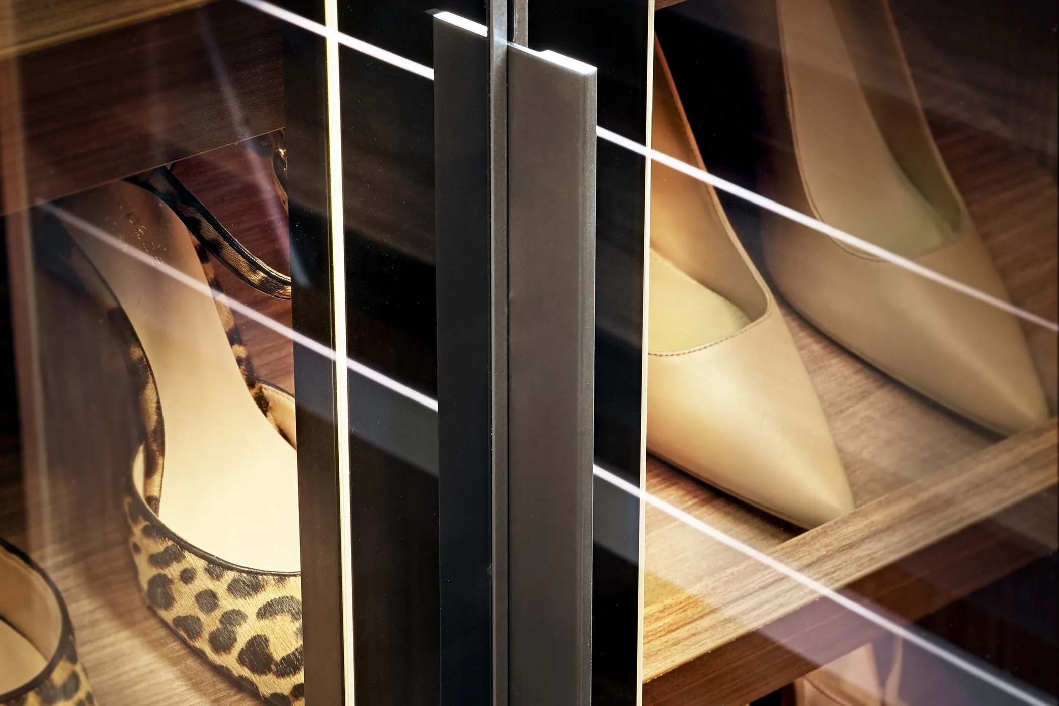 Close-up of a metal door handle on a glass wardrobe showing shoes on shelves