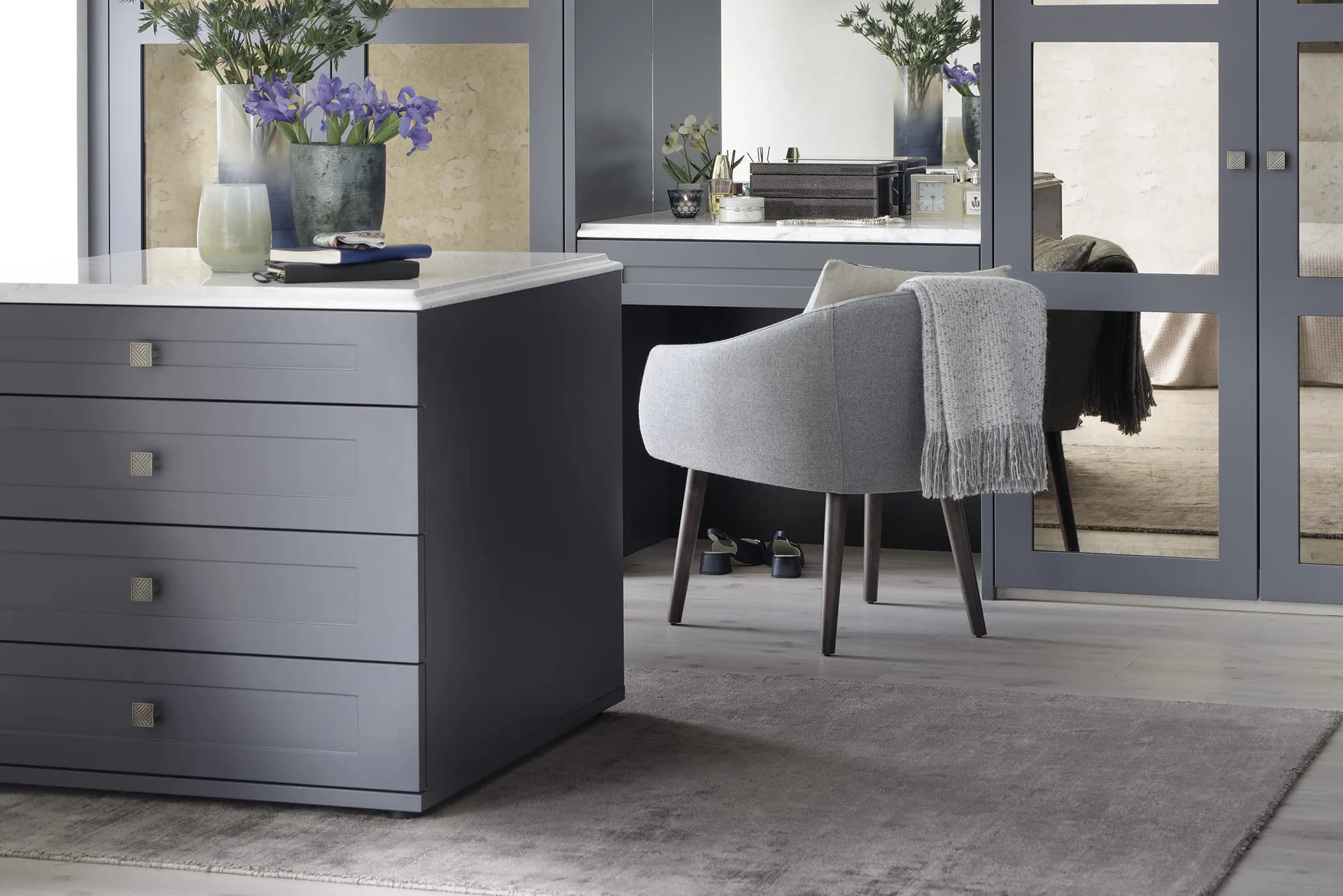 Grey dressing room island with drawers and brass handles beside mirrored wardrobe doors