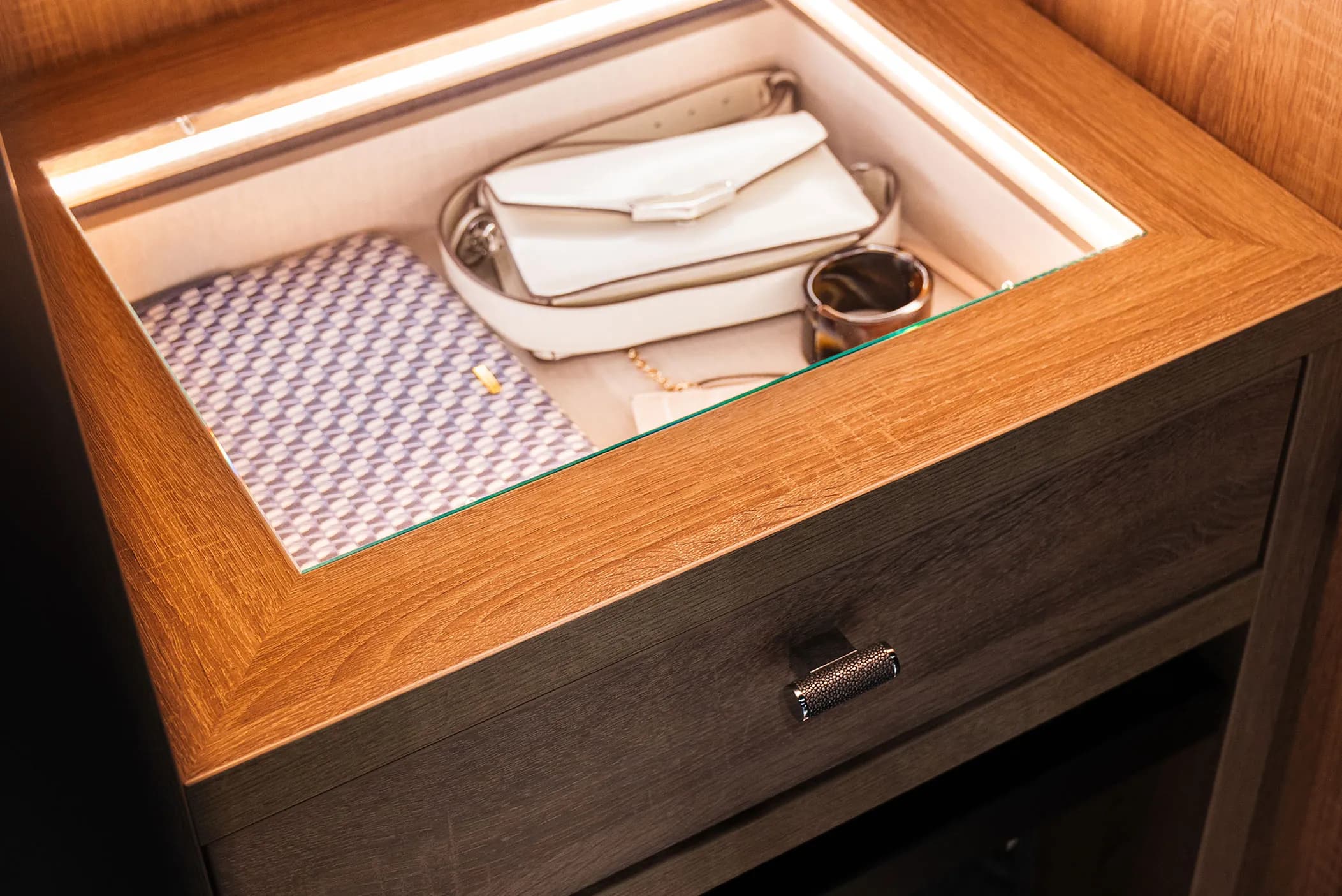 Illuminated glass-topped jewellery drawer holding handbags in an oak wardrobe