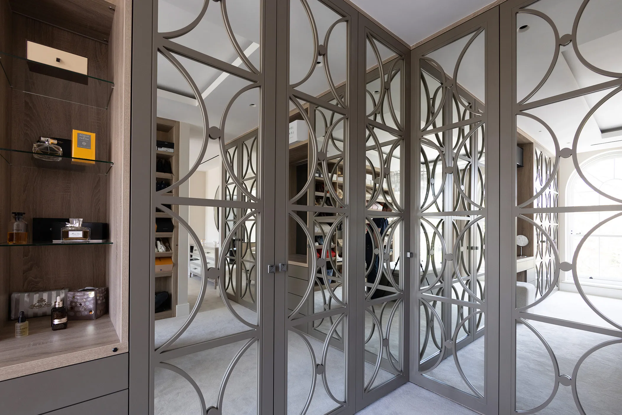 Dressing room with grey wardrobe doors featuring curved decorative mirrored panels