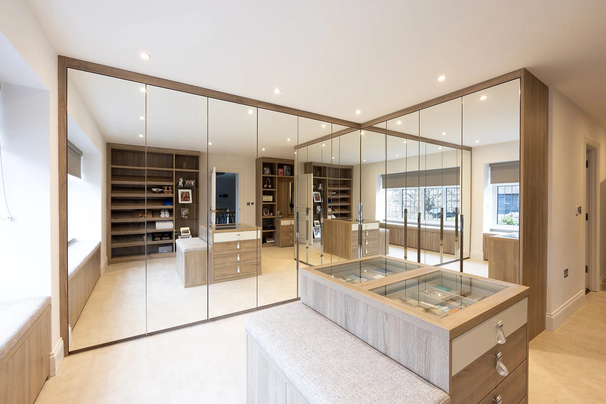 Corner dressing room with mirrored wardrobe doors, oak finish and an island unit with display top