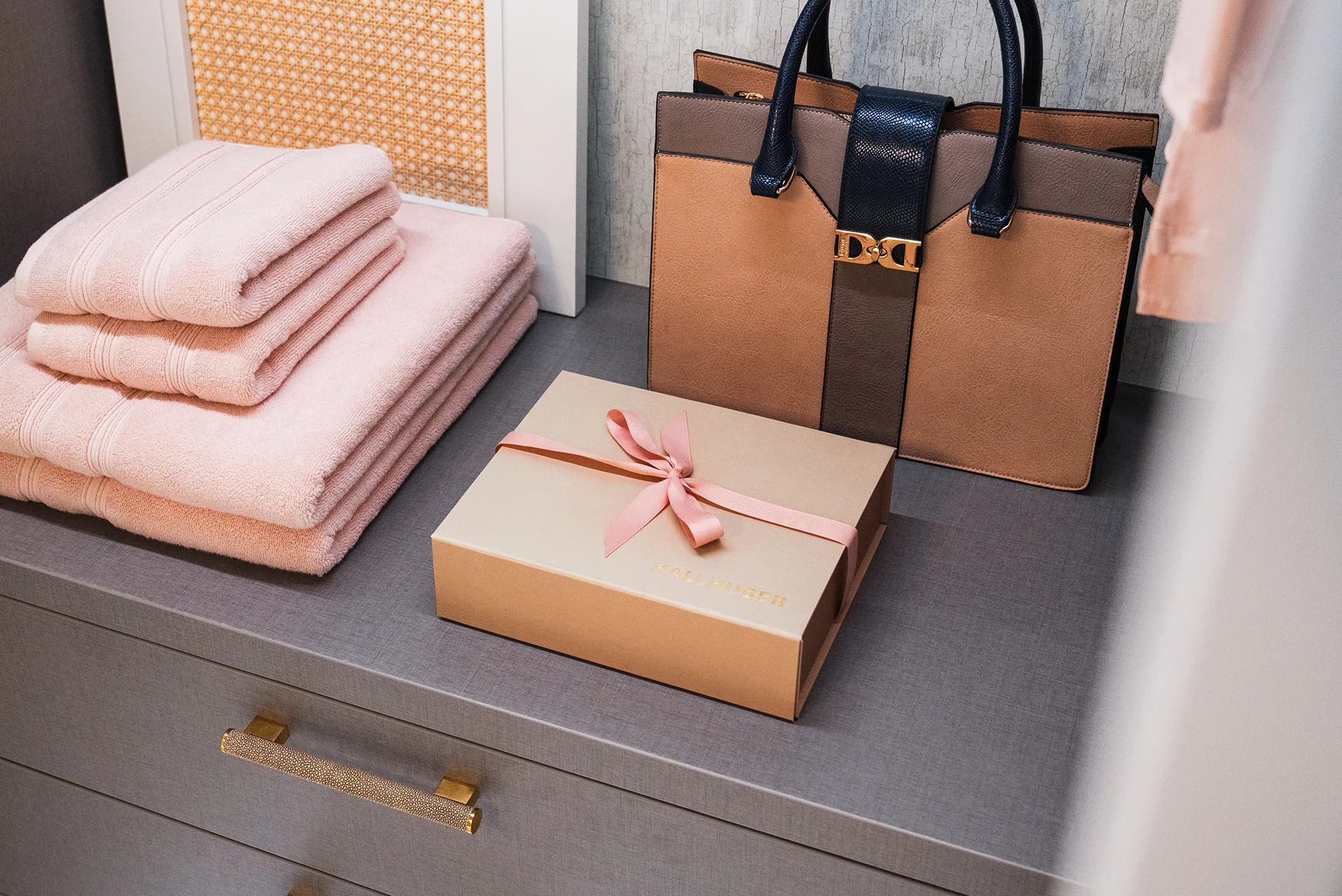 Dressing room drawer top with towels, handbag and gift box beside a brass handle