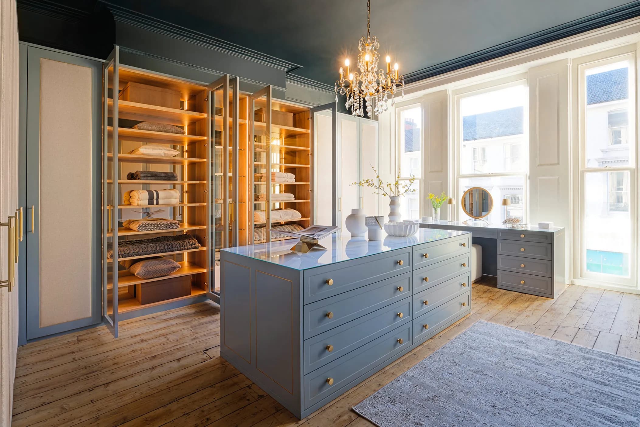 Dressing room with blue-grey island unit, glass-fronted shelving and a chandelier