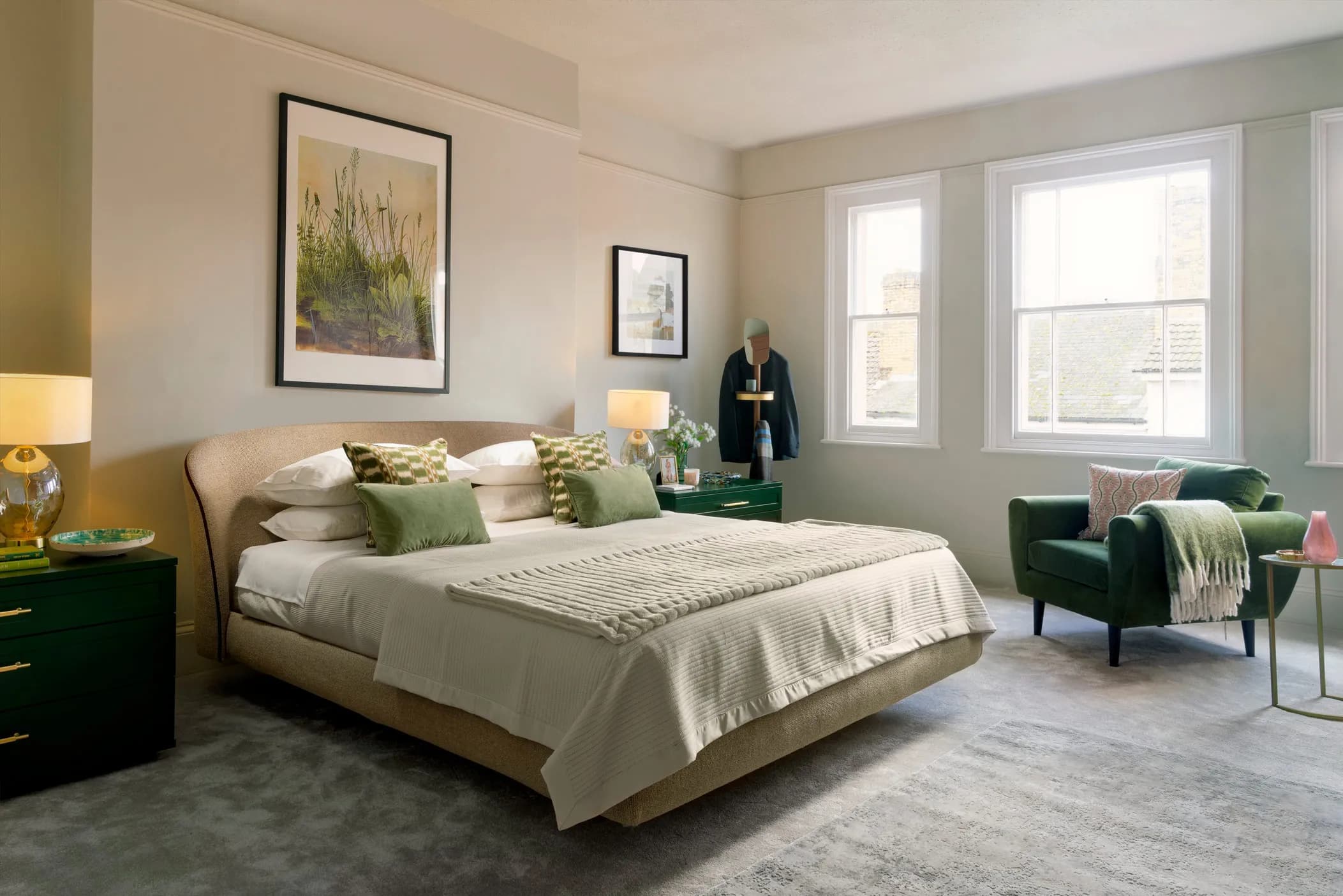 Bedroom with an upholstered bed, green bedside tables and an armchair by tall windows