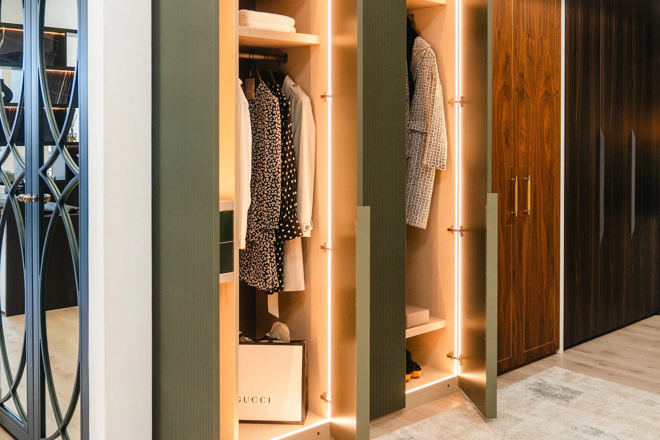 Green fluted wardrobe doors open to show lit hanging space beside walnut doors