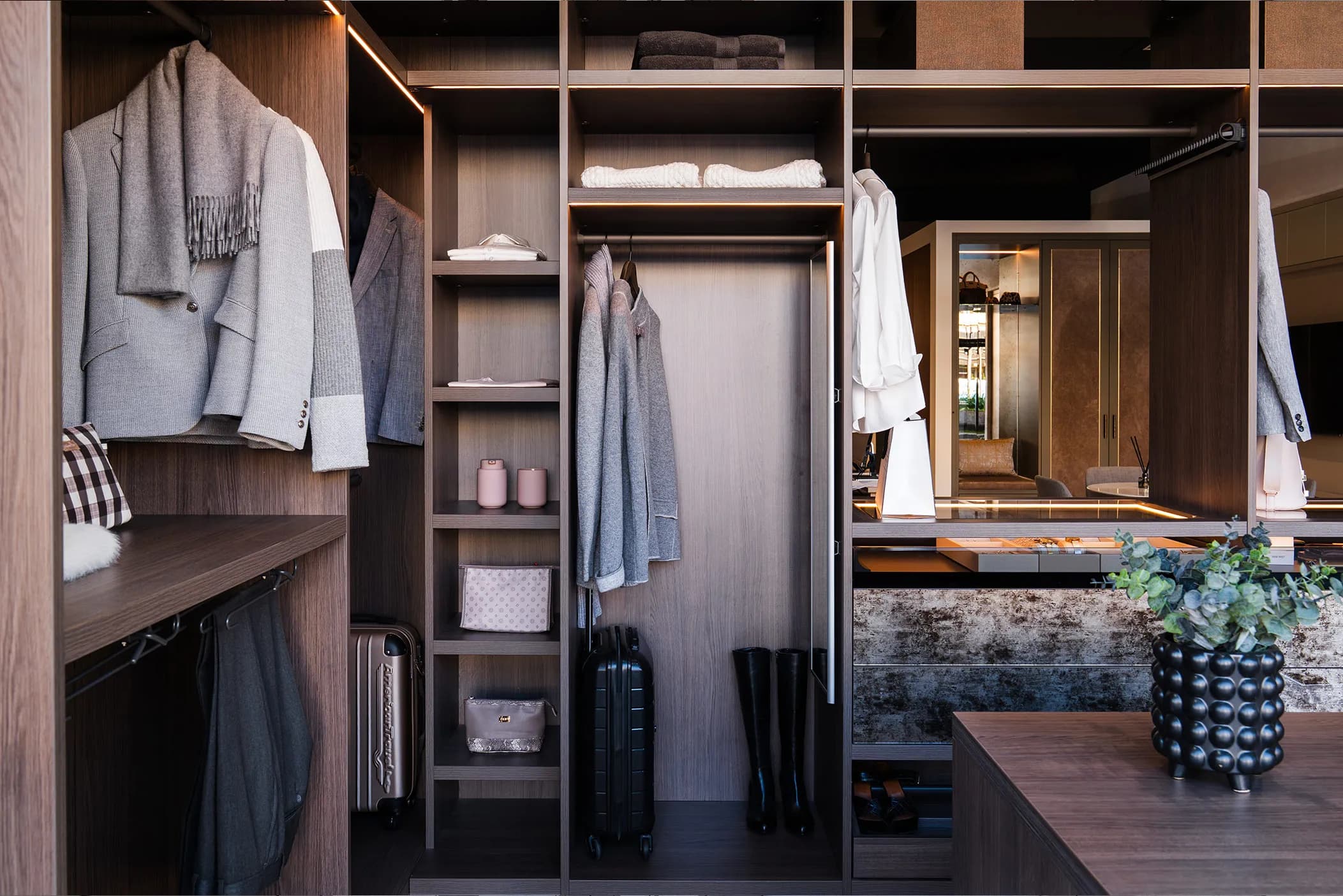 Walk-in wardrobe with open shelving, hanging rails, jackets and suitcases in warm wood