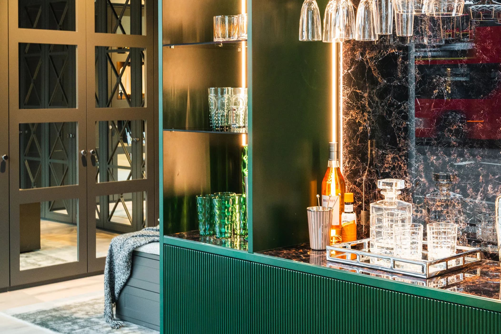 Green fluted drinks unit with glassware and a marble-effect back panel beside mirrored doors