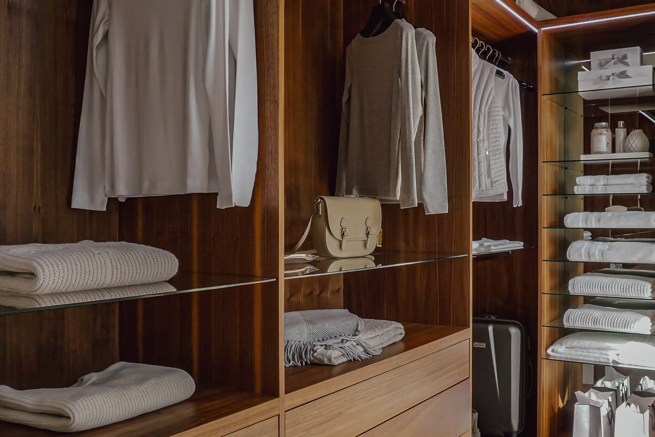 Walnut walk-in wardrobe with glass shelves, LED lighting and neatly folded clothes