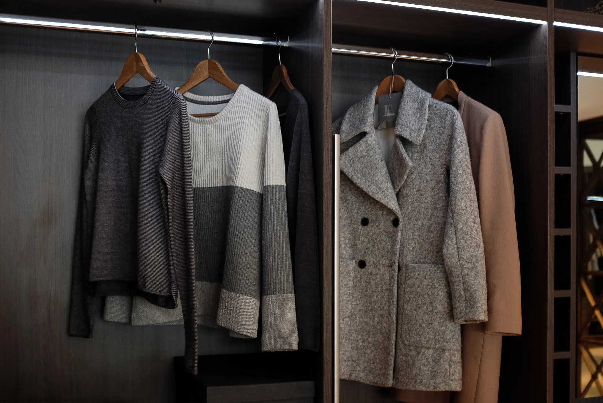 Wardrobe hanging rail with jumpers and a tweed coat under LED lighting