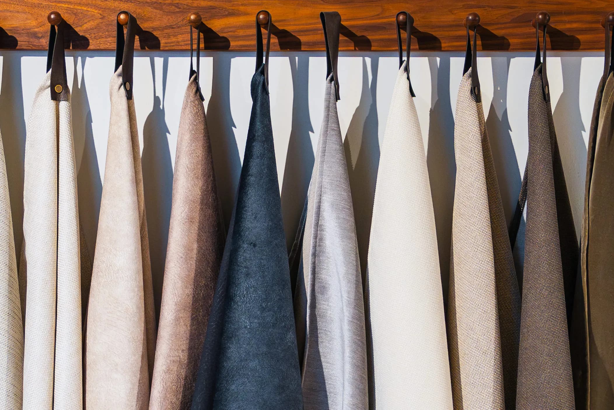 Row of fabric swatches in neutral and blue shades hanging from a wooden rail