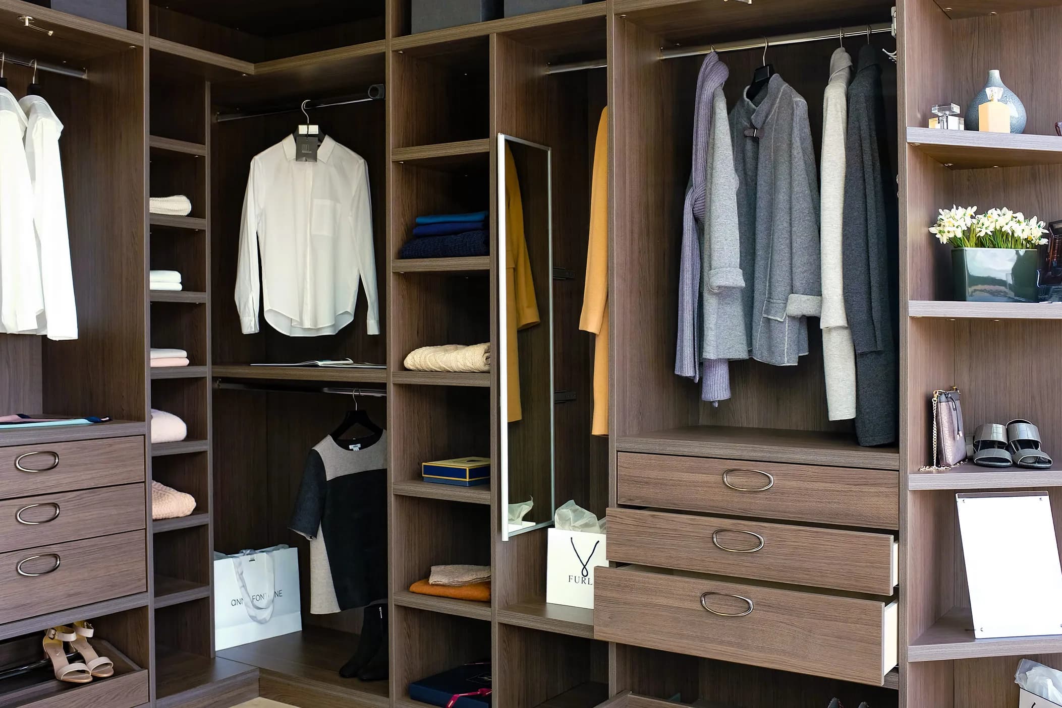 Corner walk-in wardrobe with oak-effect shelves, drawers, hanging clothes and a mirror