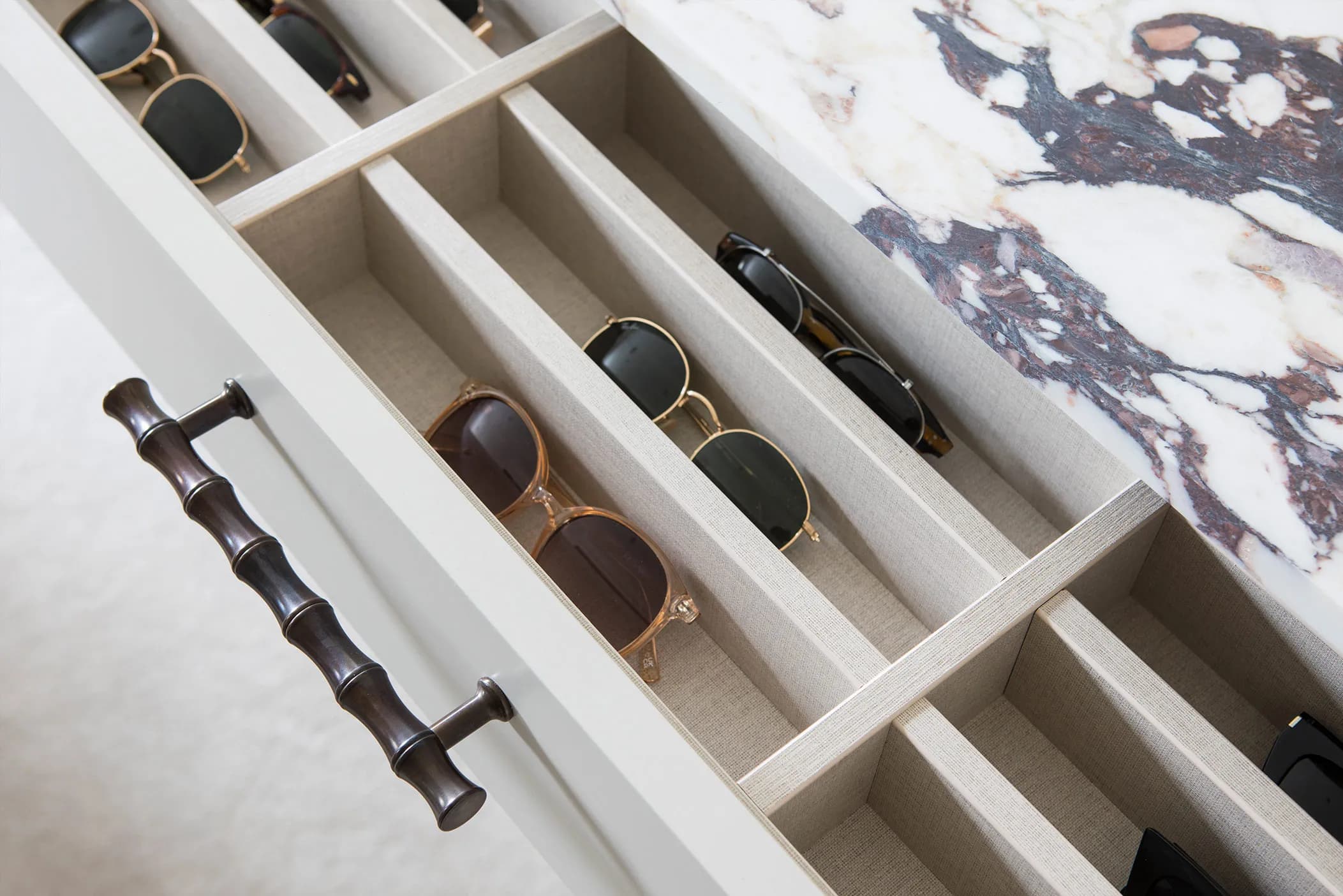 Open wardrobe drawer with sunglasses in dividers, a bamboo-style handle and marble top