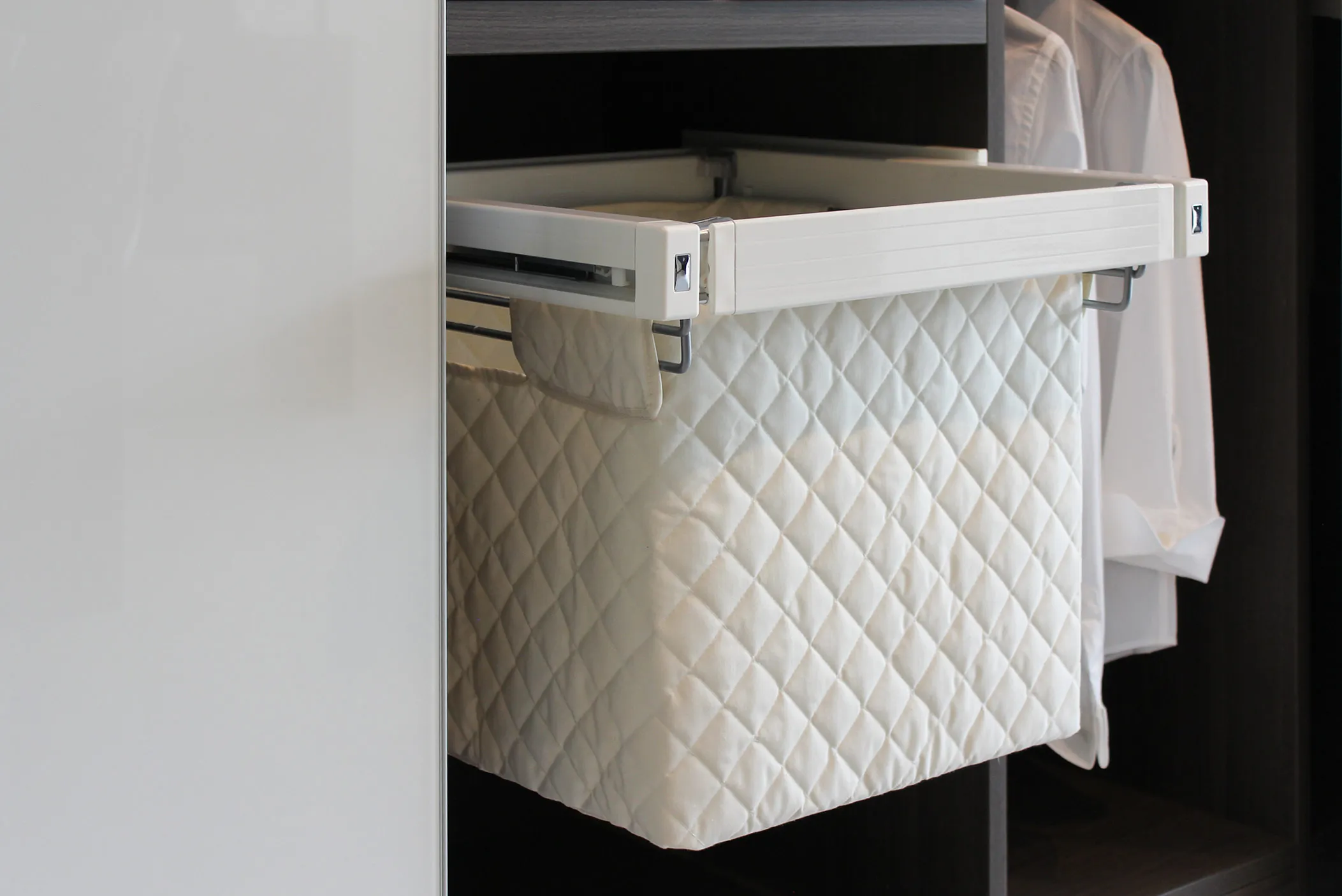 Pull-out quilted laundry basket in a wardrobe beside hanging shirts