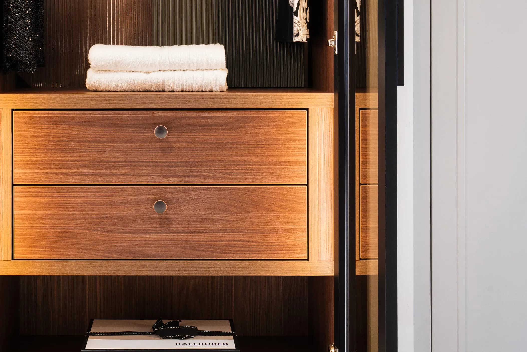 Walnut drawer unit with round handles and folded towels inside a wardrobe