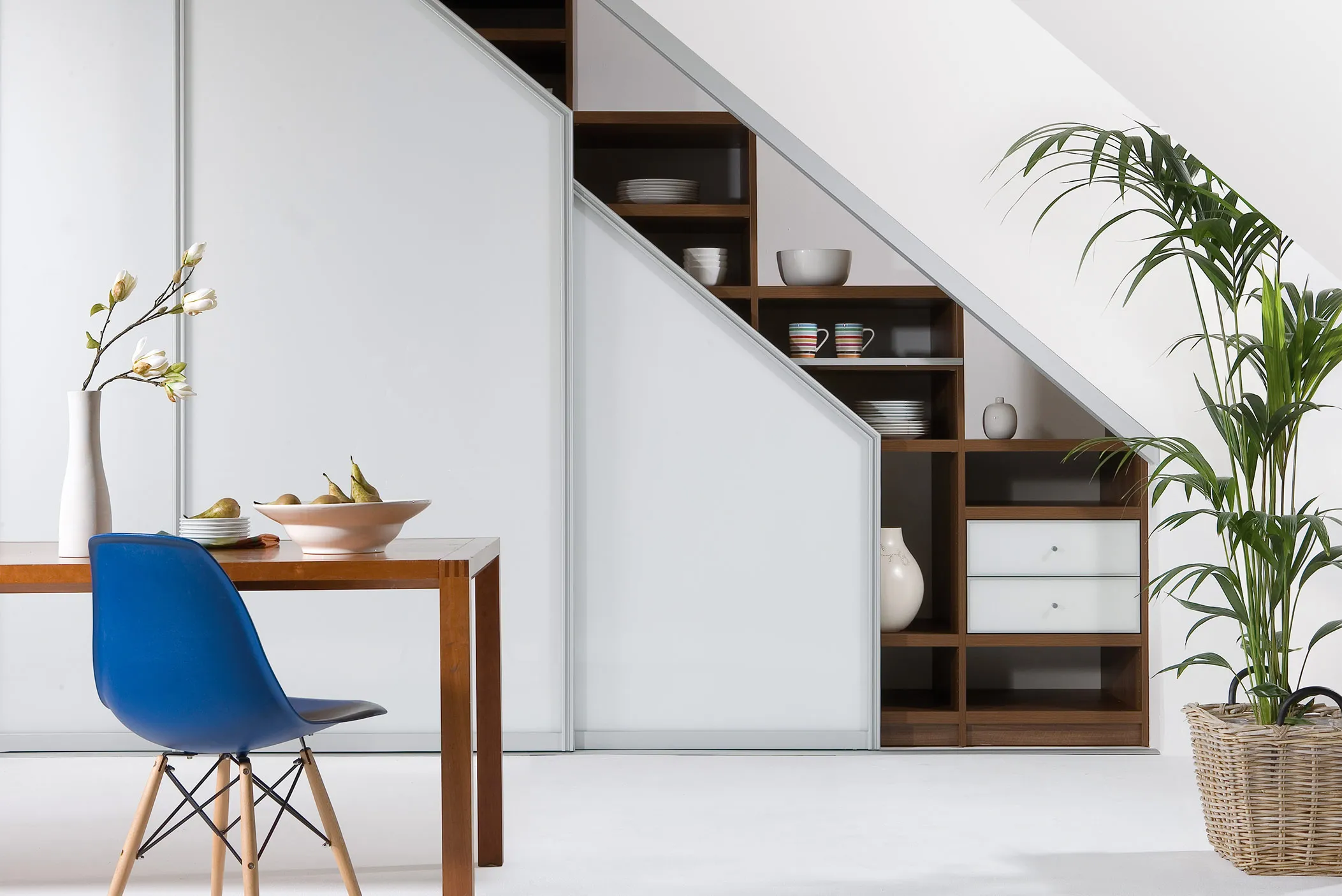 Under-stairs sliding door wardrobe with white doors and walnut shelving, dining table and blue chair