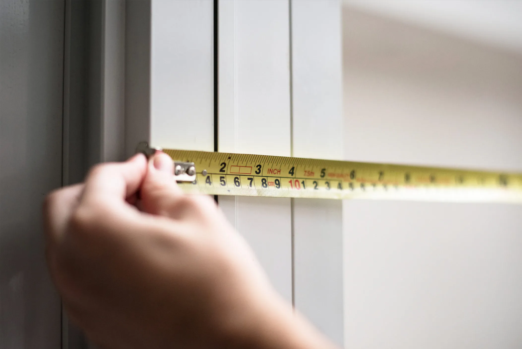 Hand holding a tape measure against a white wardrobe door frame