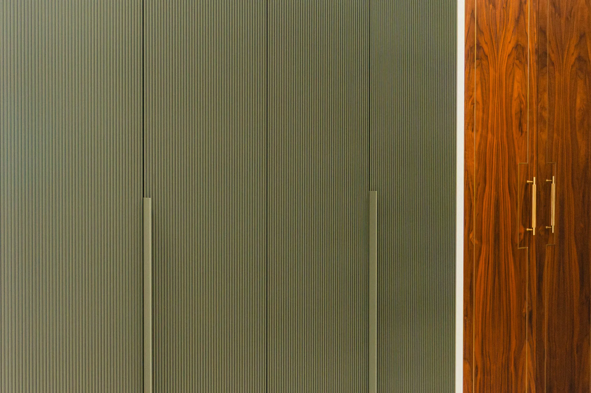 Fluted green wardrobe doors with long handles beside walnut veneer doors with brass handles