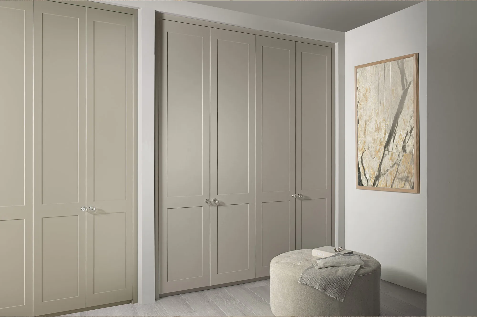 Pale grey Shaker-style fitted wardrobes with an ottoman and framed artwork