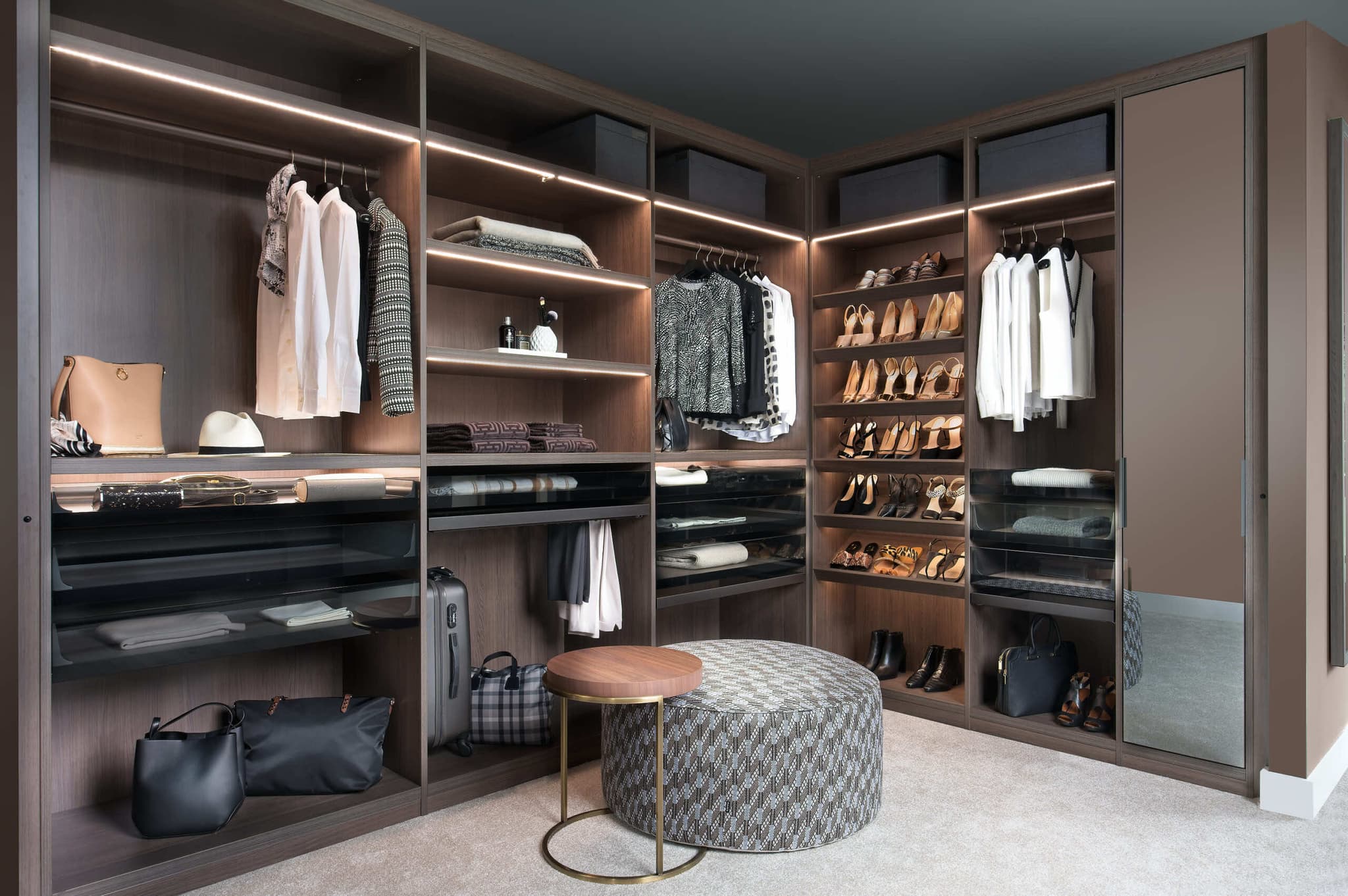 Dark wood corner walk-in wardrobe with shoe shelves, LED lighting and a patterned ottoman