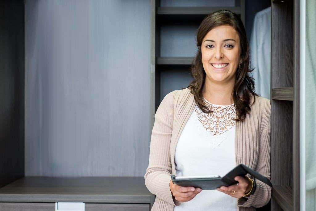 Smiling woman holding a tablet in front of a fitted wardrobe