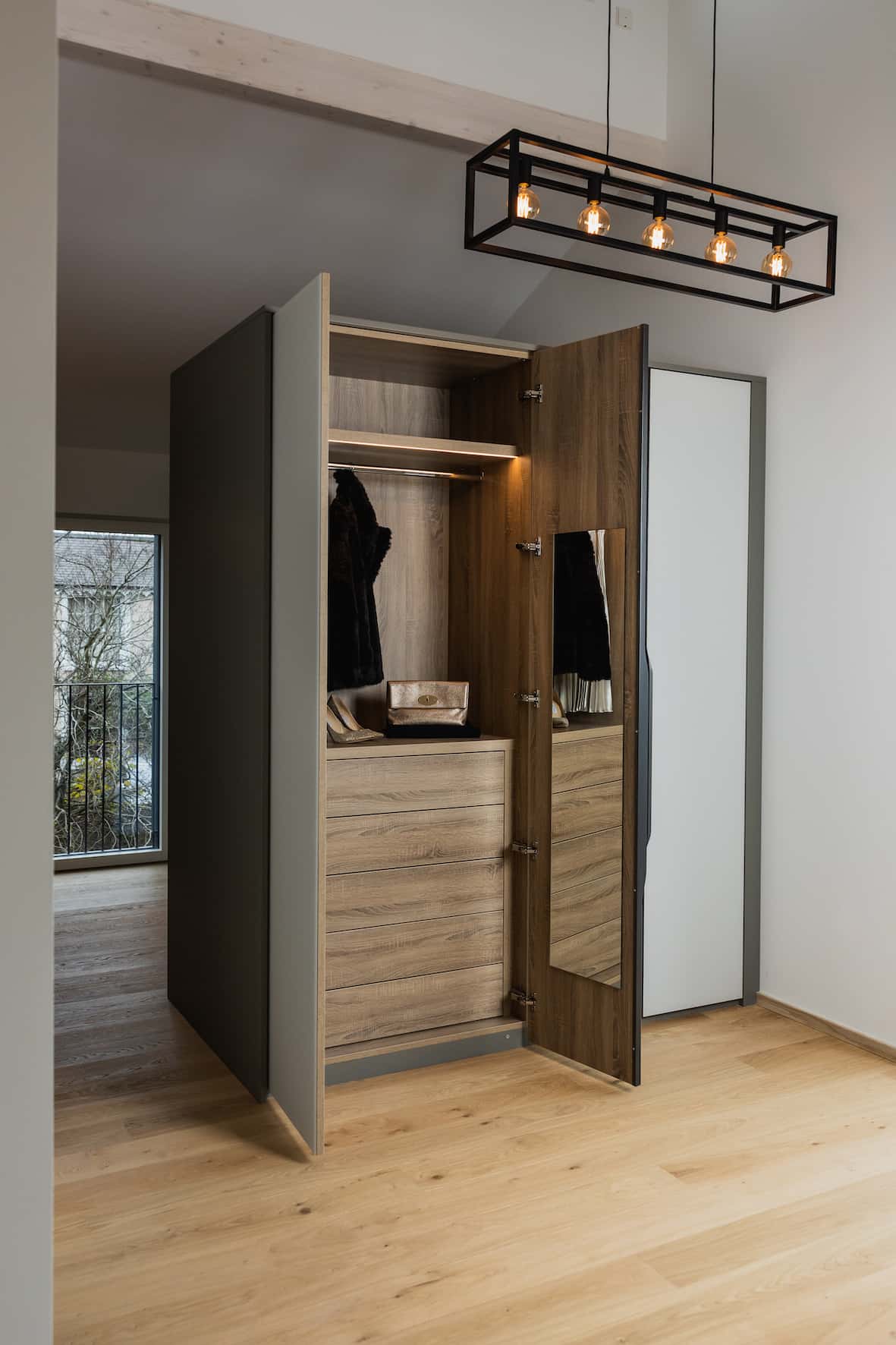 Open wardrobe with oak-effect interior, drawers and hanging space under a pendant light