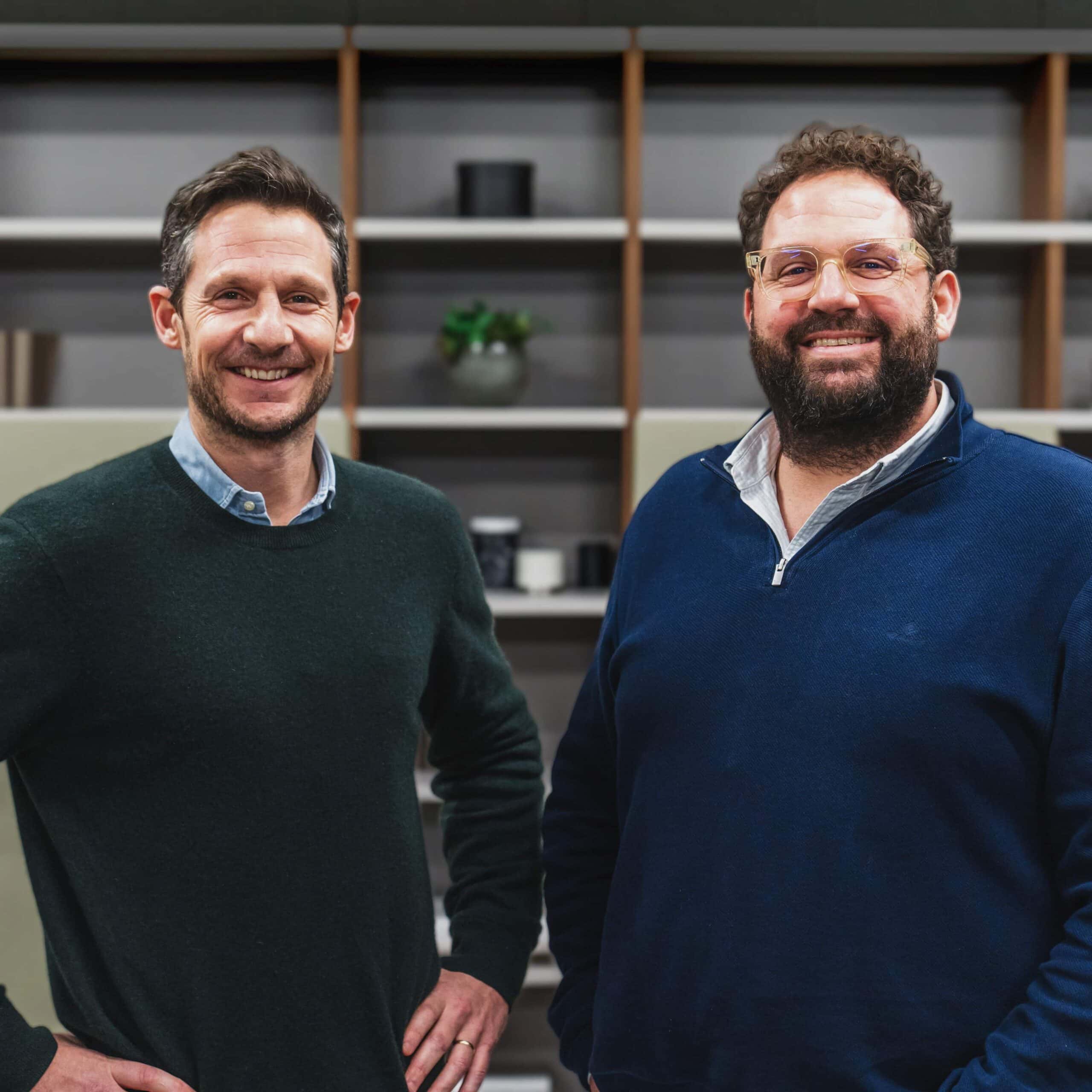 Two smiling men standing together in front of fitted shelving