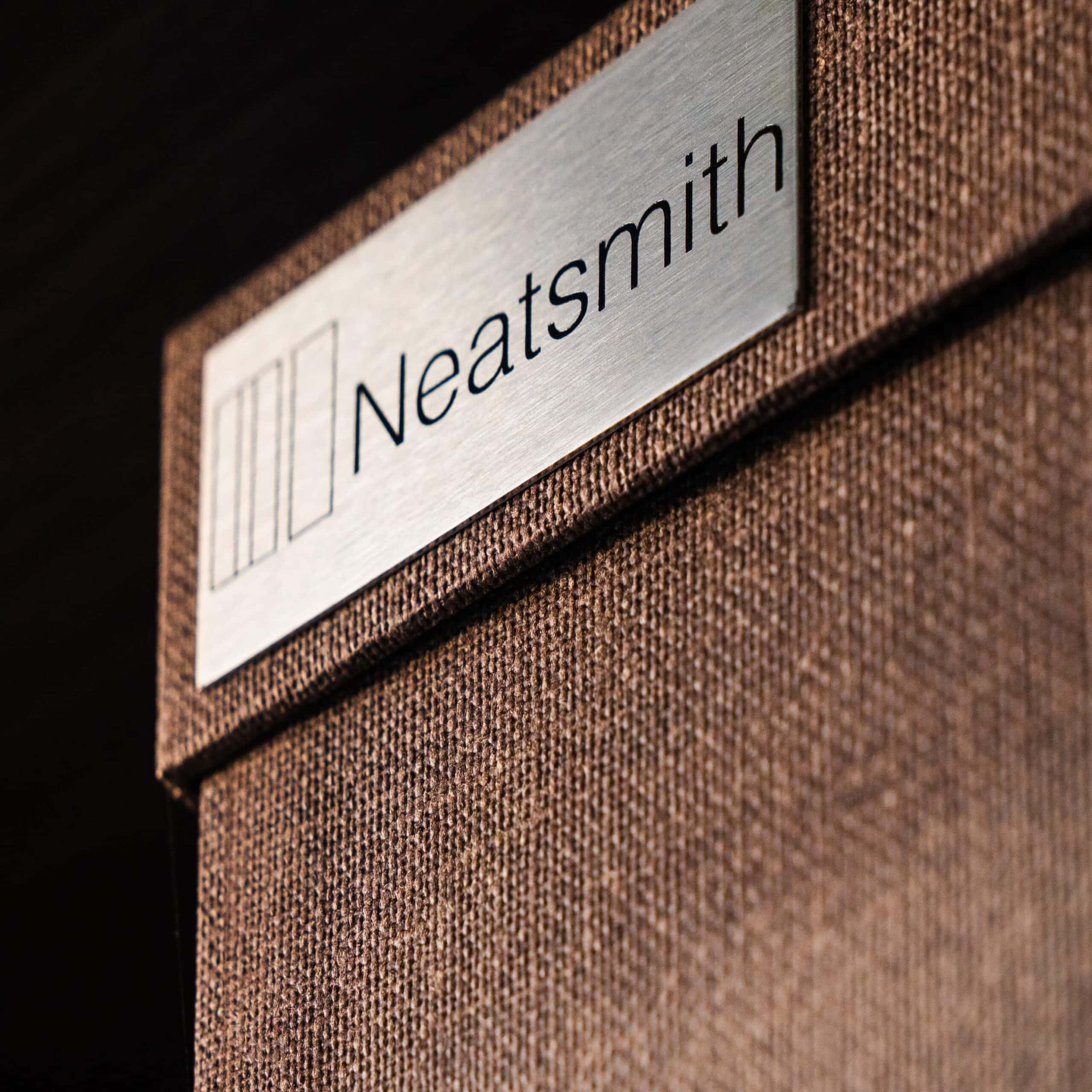 Neatsmith logo plate on a brown linen-textured wardrobe door