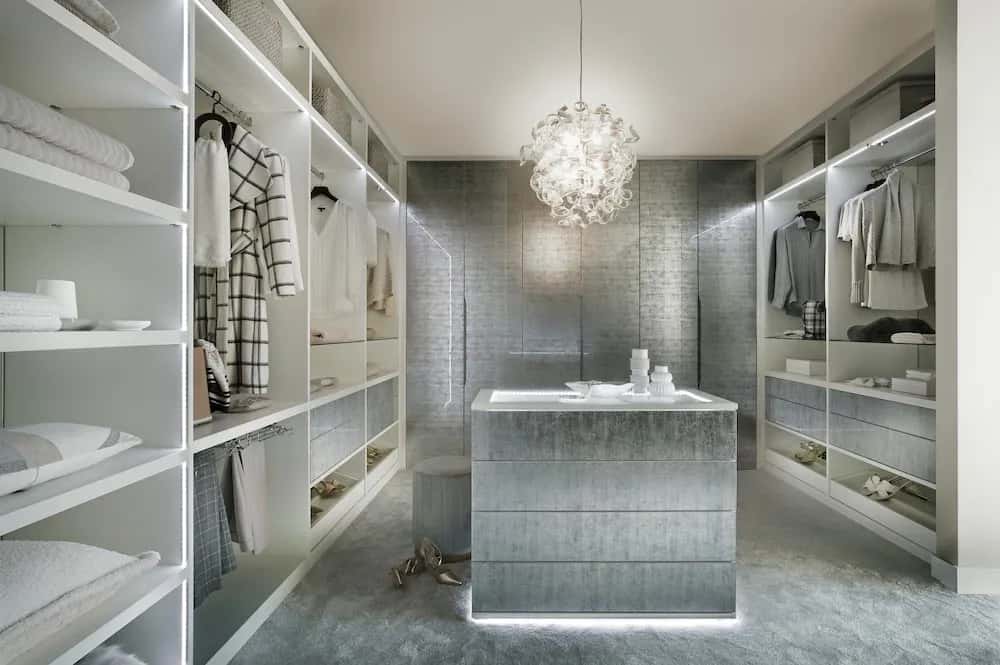 Walk-in wardrobe with decorative glass doors, LED-lit shelving, island unit and chandelier