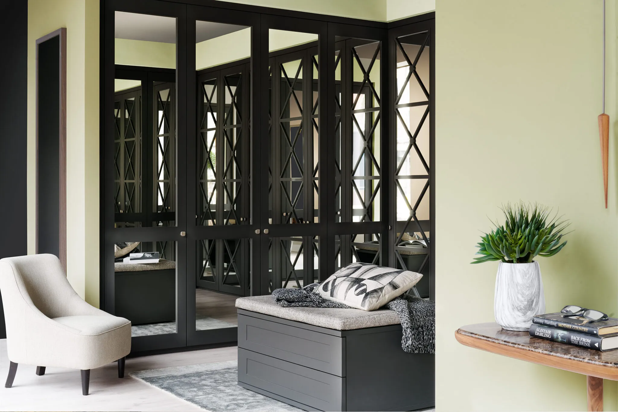 Black fitted wardrobe with cross-pattern mirrored doors beside a bench and green wall