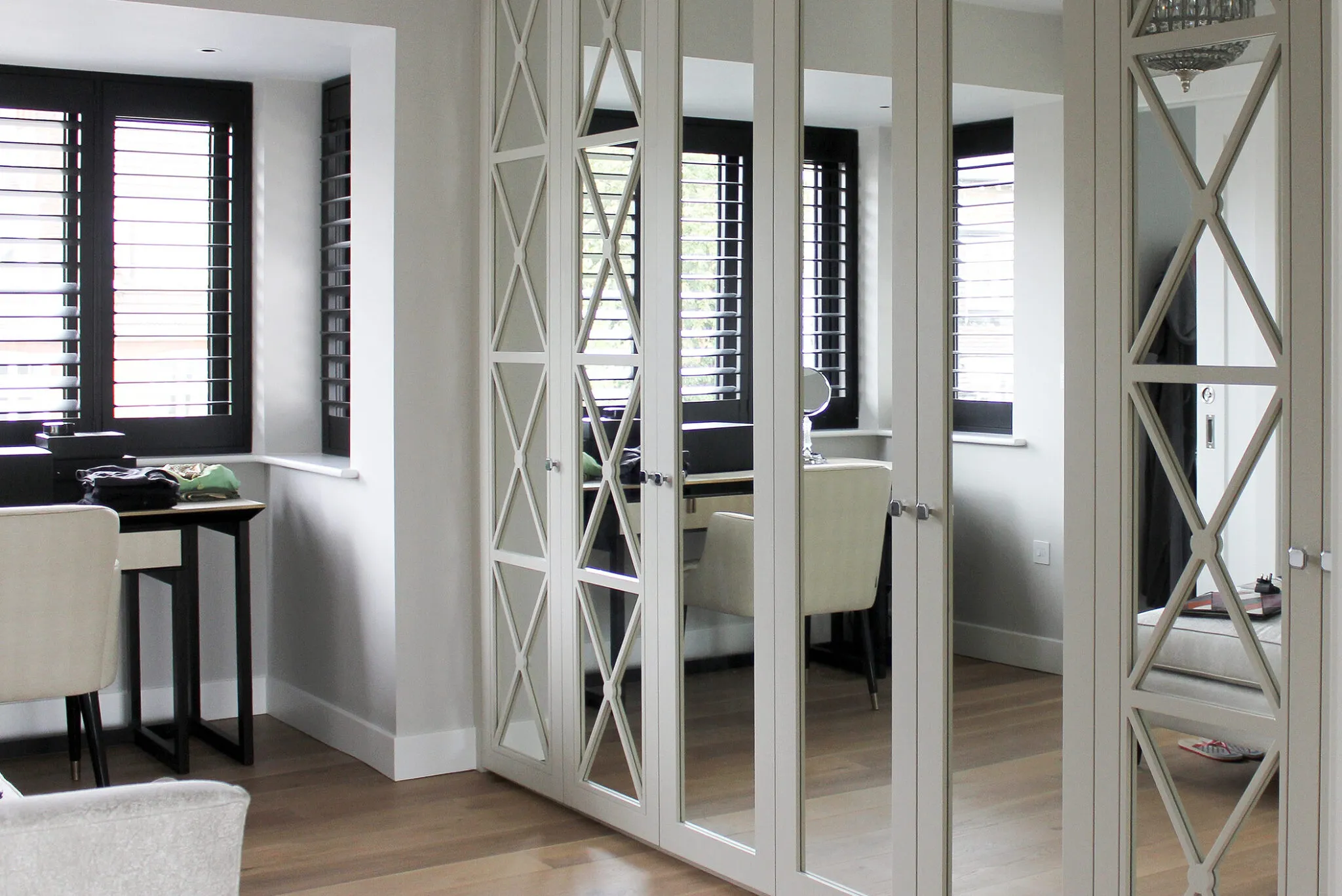 Fitted wardrobe with mirrored doors and cross-pattern glazing bars beside a window with shutters
