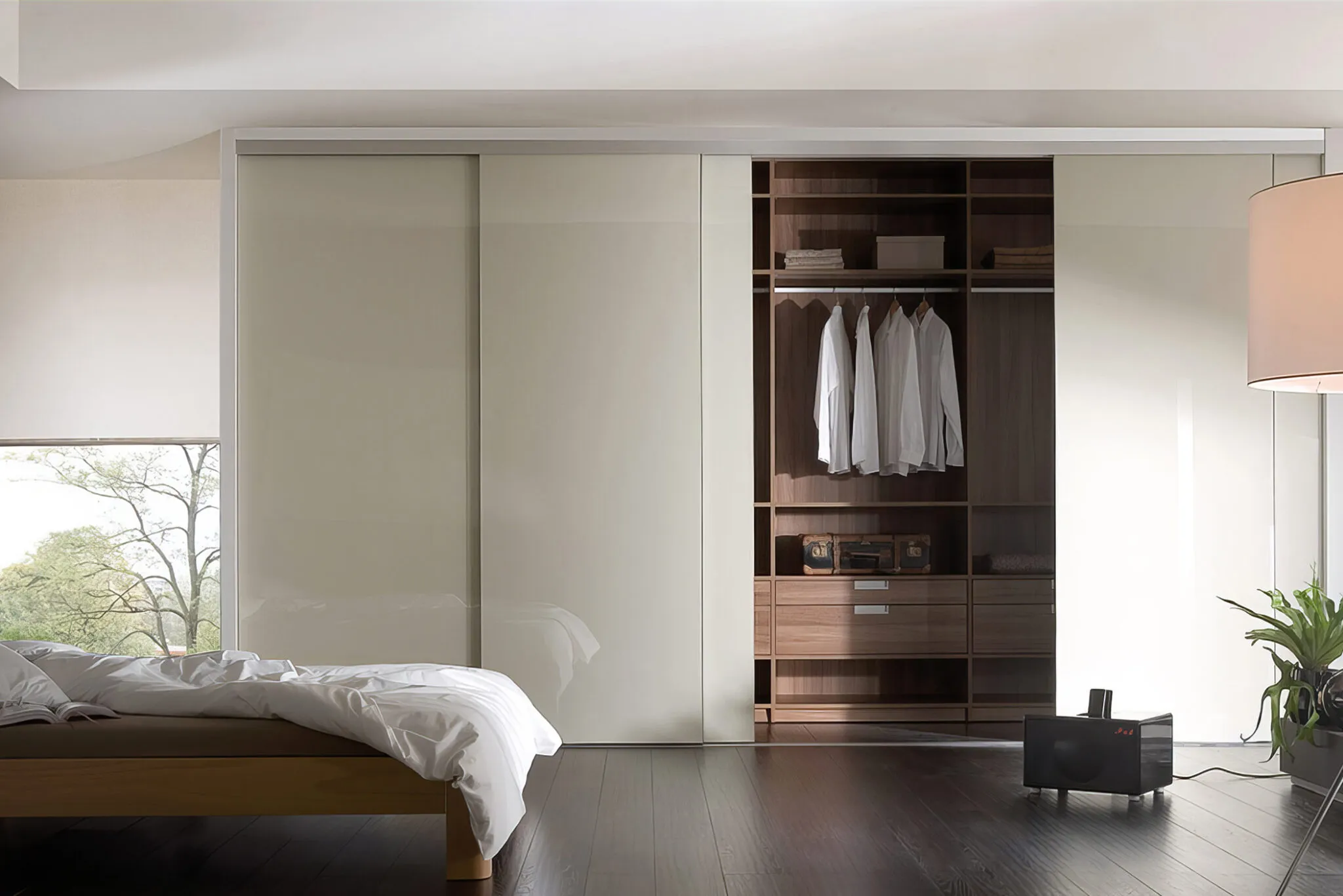 Cream glass sliding-door fitted wardrobe with walnut interior beside a low bed