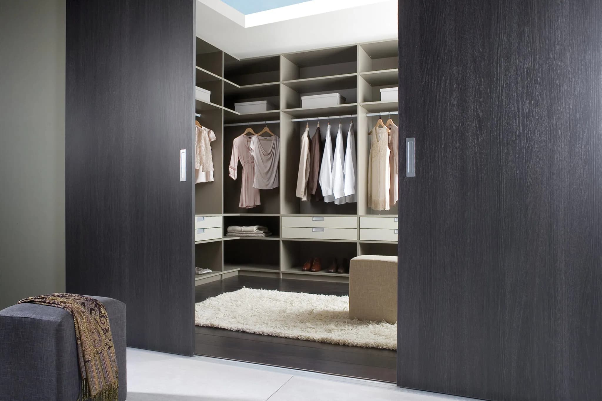 Walk-in wardrobe with dark sliding doors open to reveal white shelving and hanging space