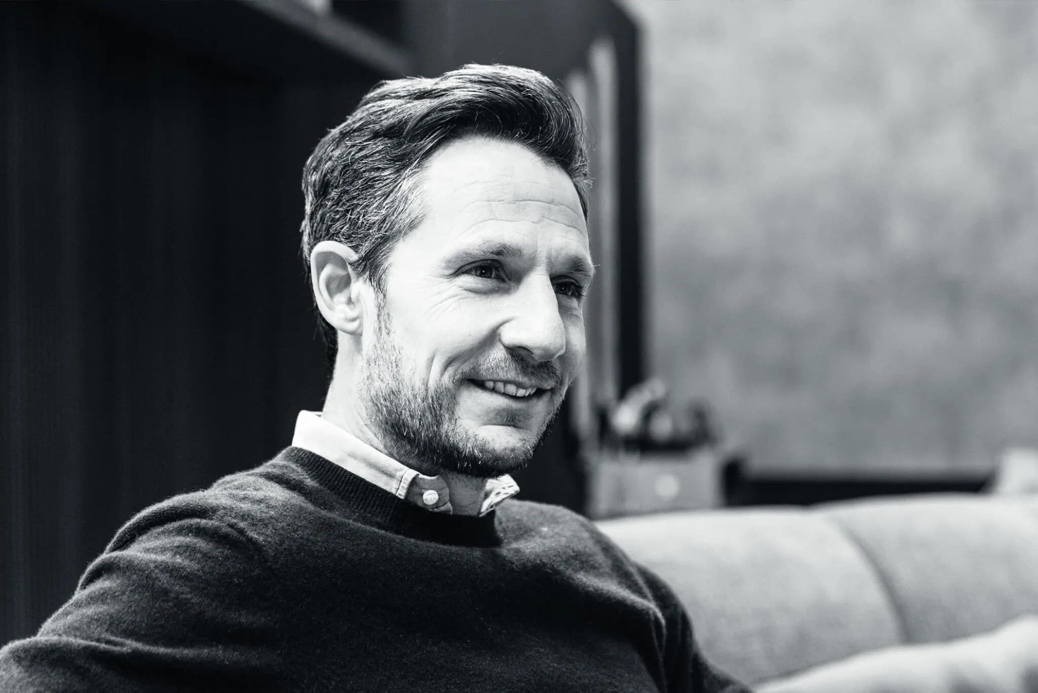 Black and white portrait of a smiling man seated on a sofa