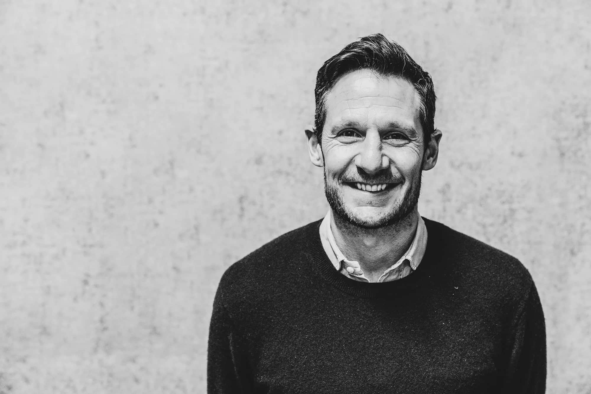 Black and white portrait of a smiling man in a dark jumper